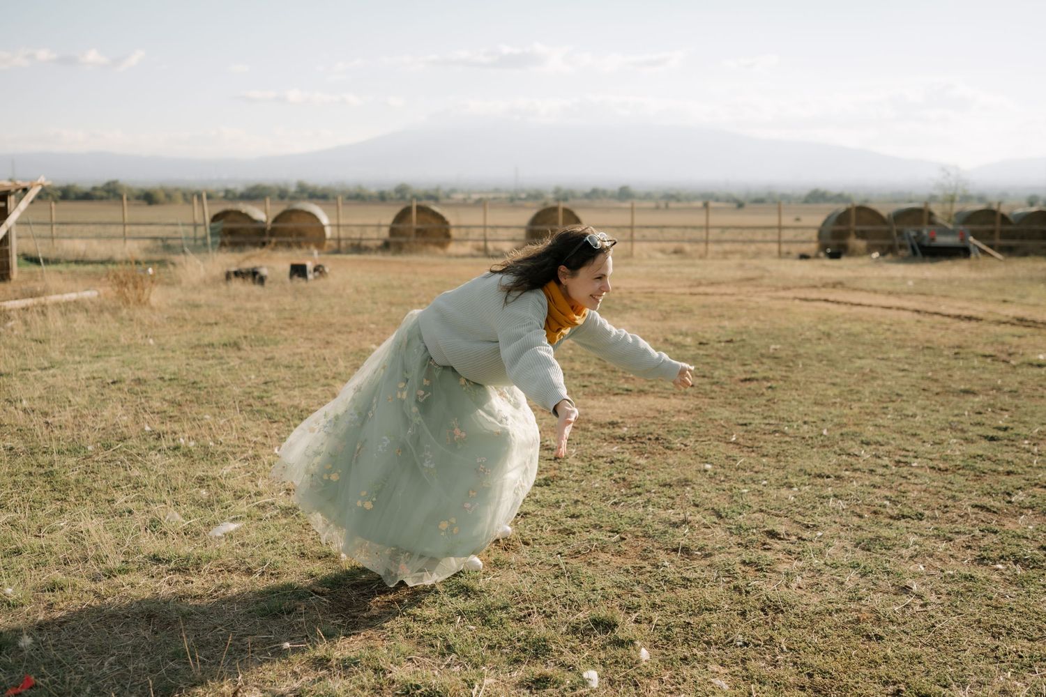 A person in a flowing white dress runs gracefully through a golden field at sunset creating an ethereal scene.