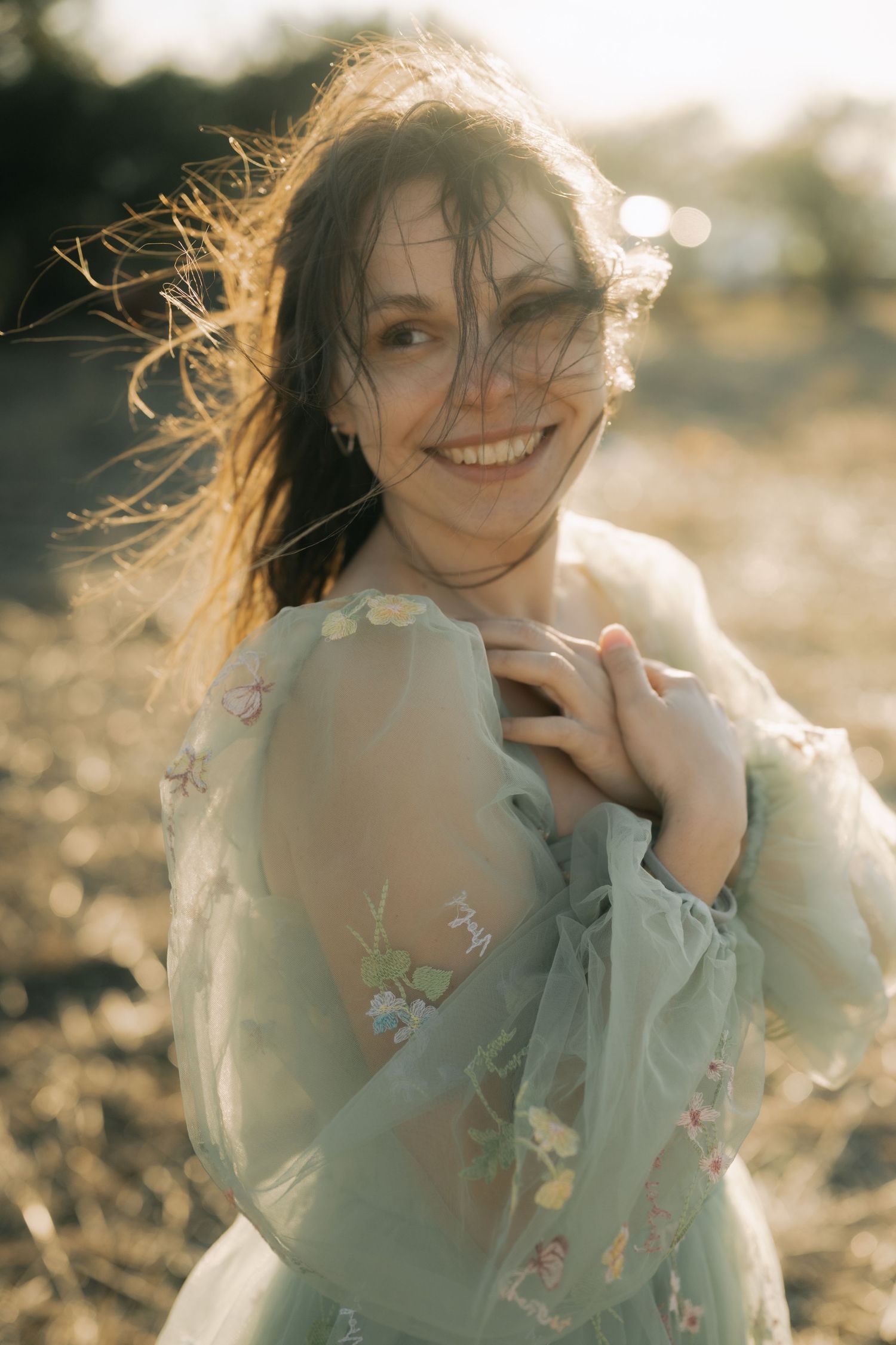 Dreamy outdoor portrait series showing windswept hair and delicate floral embroidered dress in golden sunlight.
