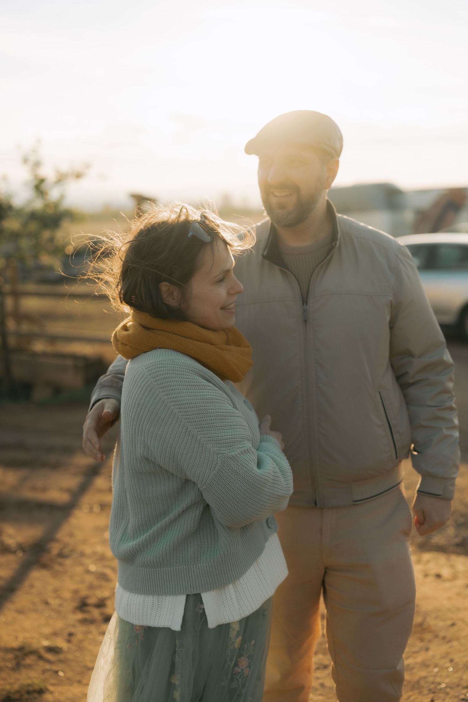 A couple embraces during golden hour on a rural dirt path as sunlight creates a warm glow around them.