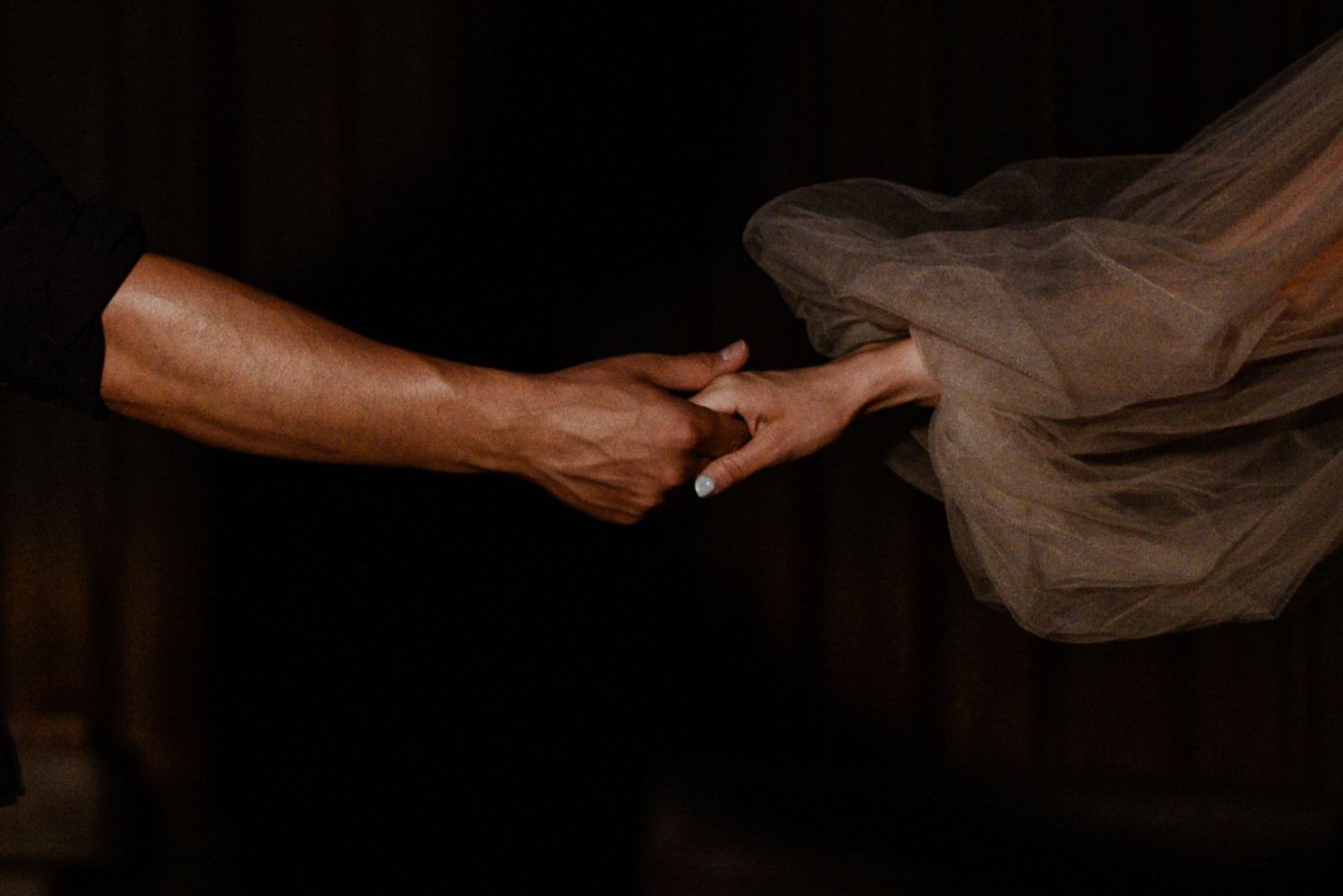 A hand gently holds flowing sheer fabric against a dark background creating an ethereal effect.