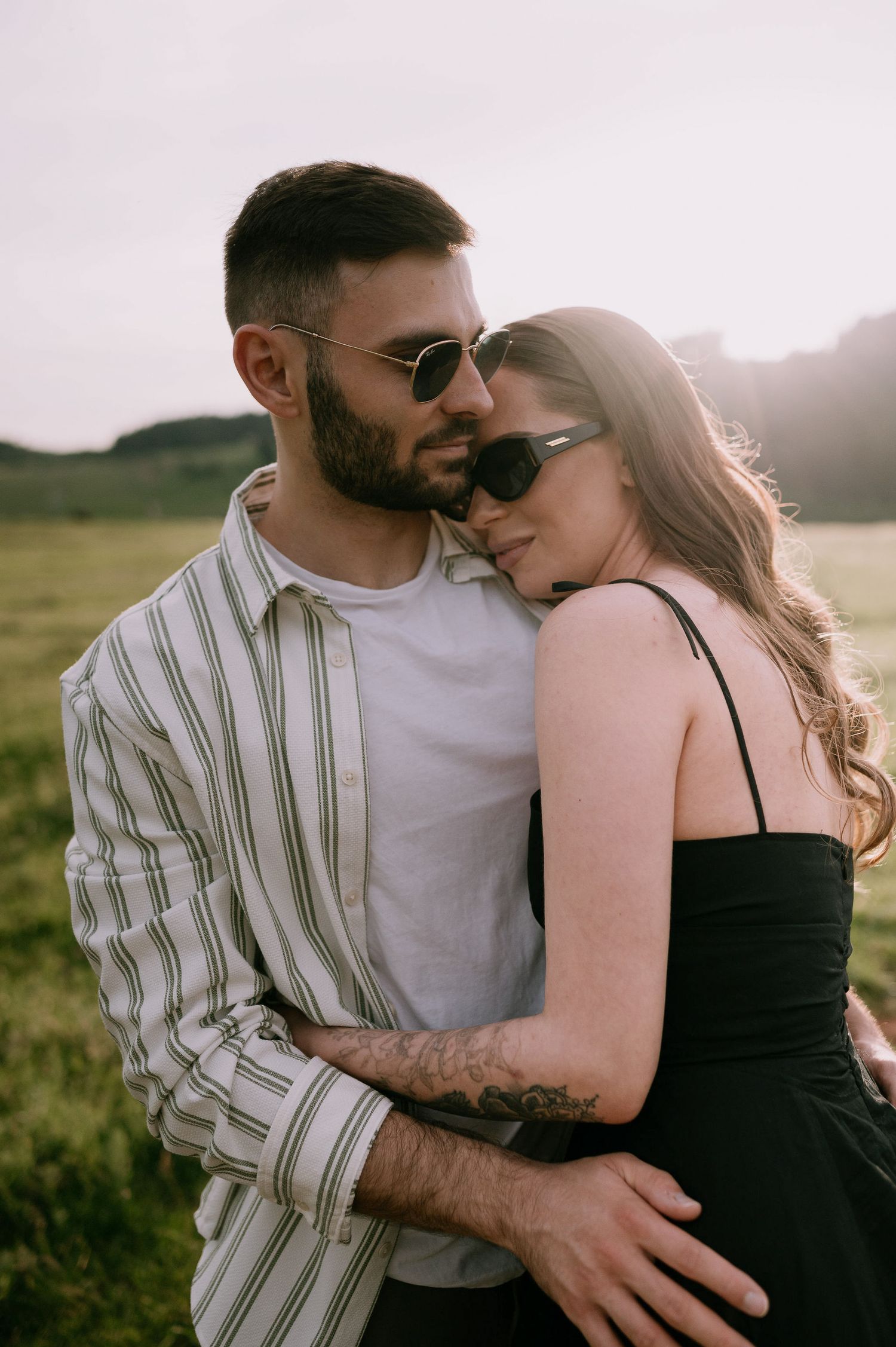 A romantic couple embraces in a sunlit field wearing black and striped clothing during golden hour.