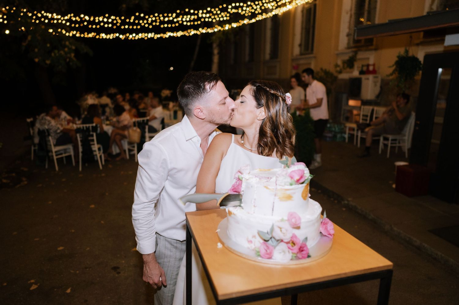 A romantic wedding couple shares intimate moments under twinkling lights at their evening reception celebration.