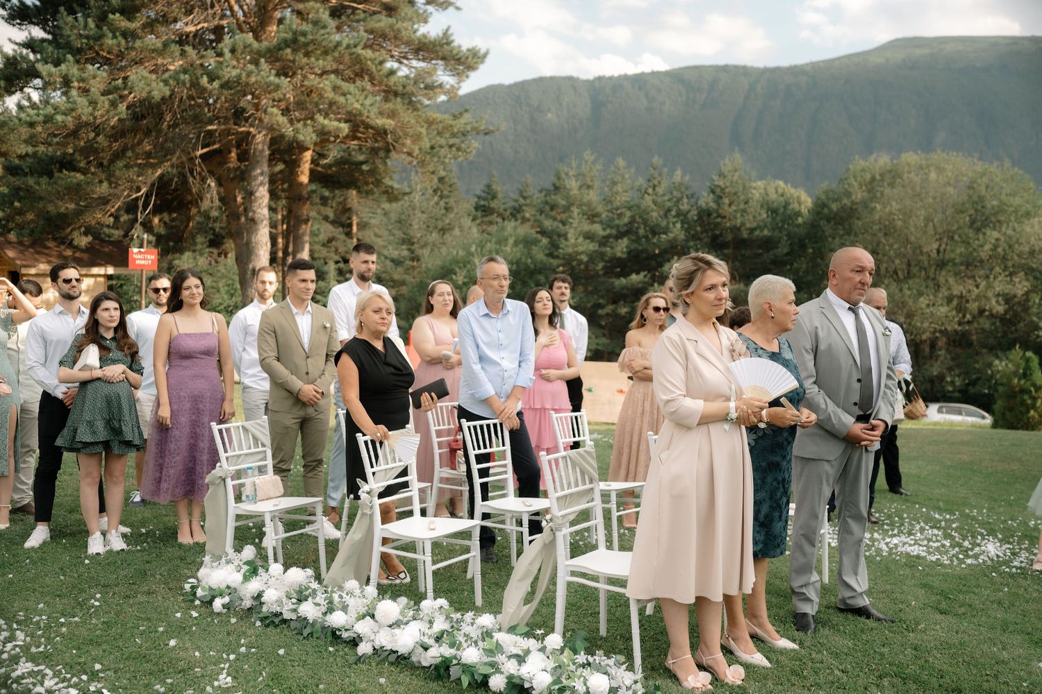 Wedding ceremony setup with white chairs on a grassy hillside overlooking mountains and forest scenery.