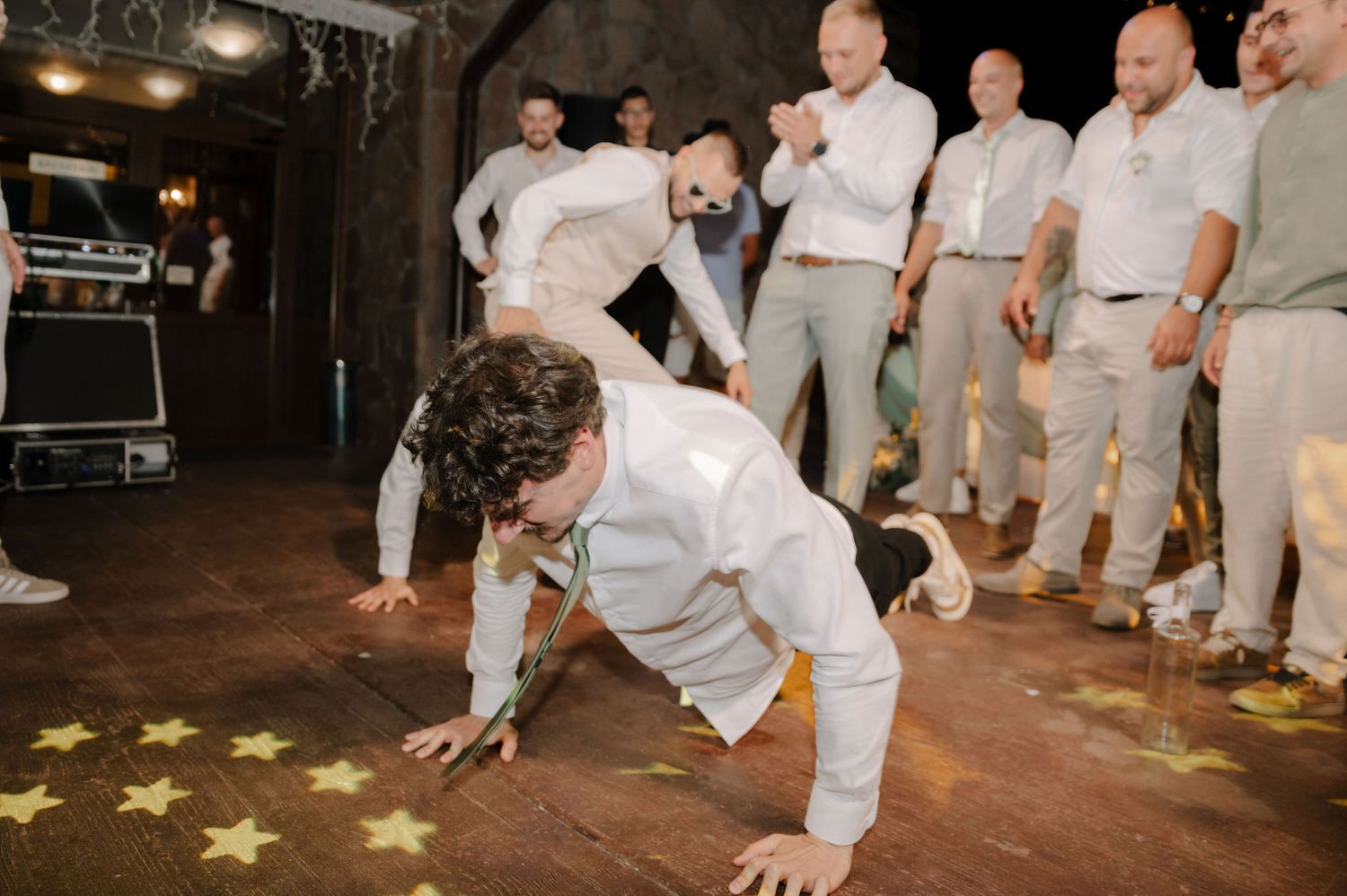 Wedding party in white attire dancing and celebrating on a dance floor with star decorations.