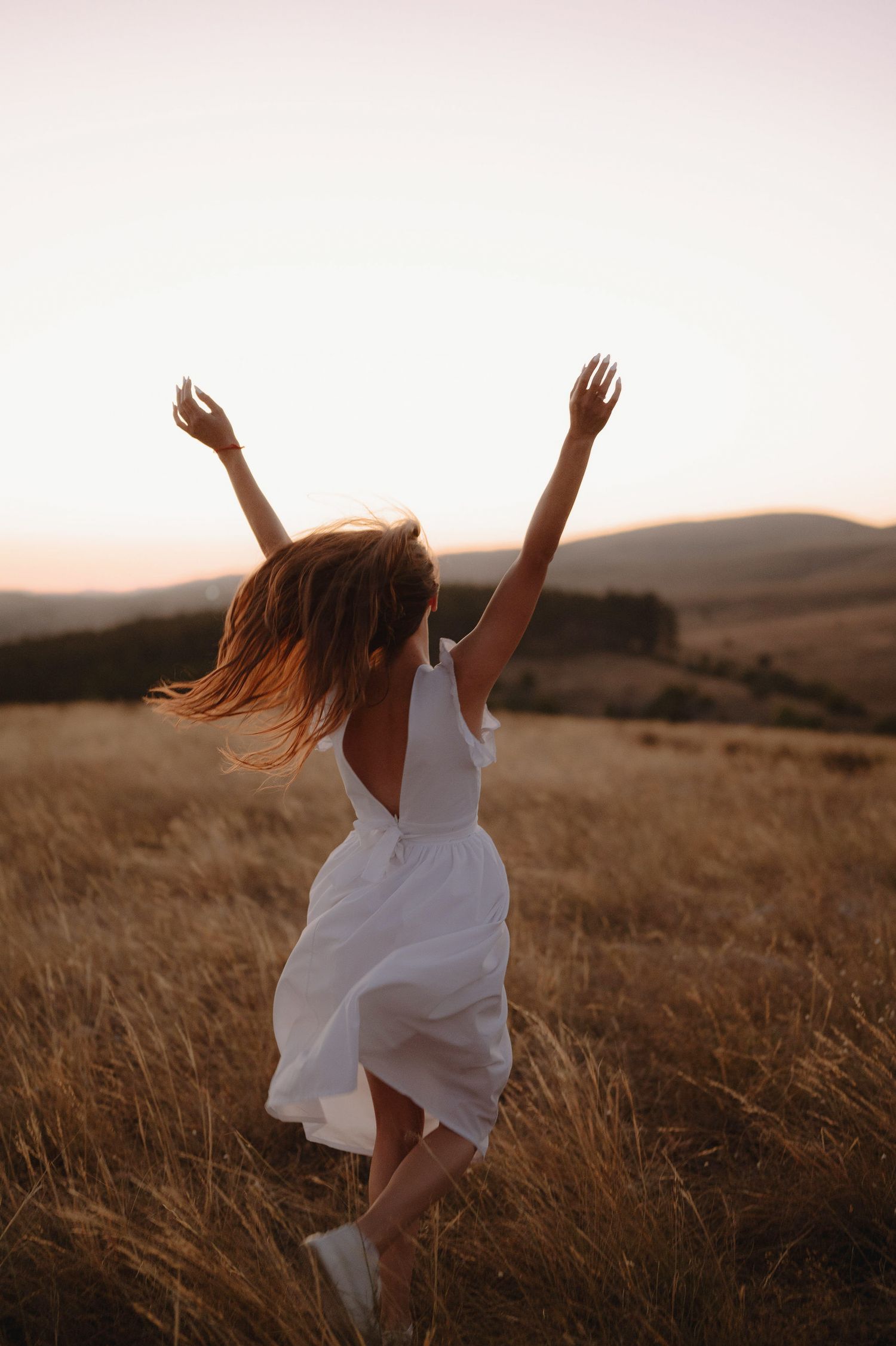 A figure in a flowing white dress dances freely through a golden field at sunset, hair flowing in the wind.