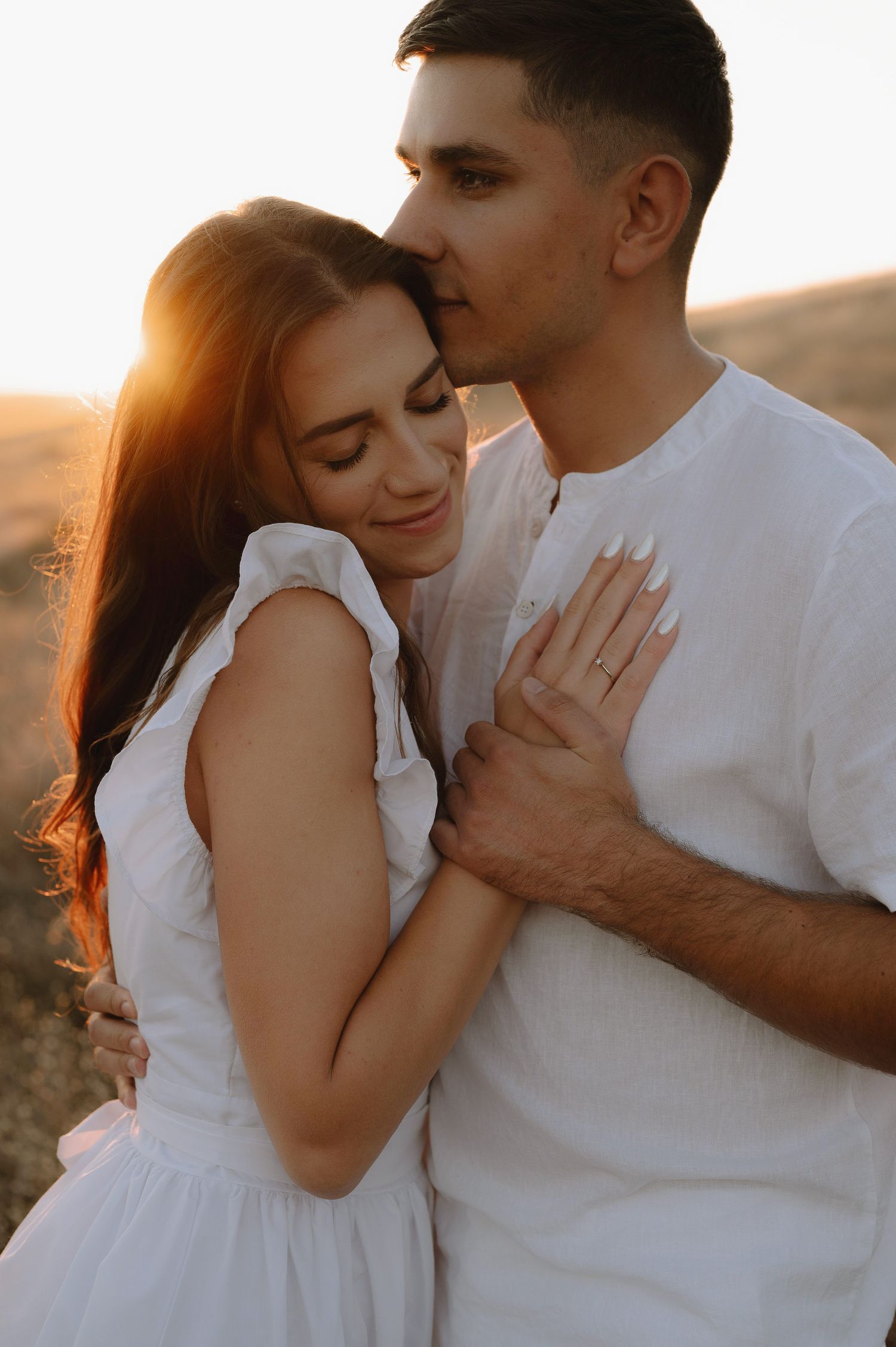 Two people share intimate moments in white clothing against a warm sunset backdrop.