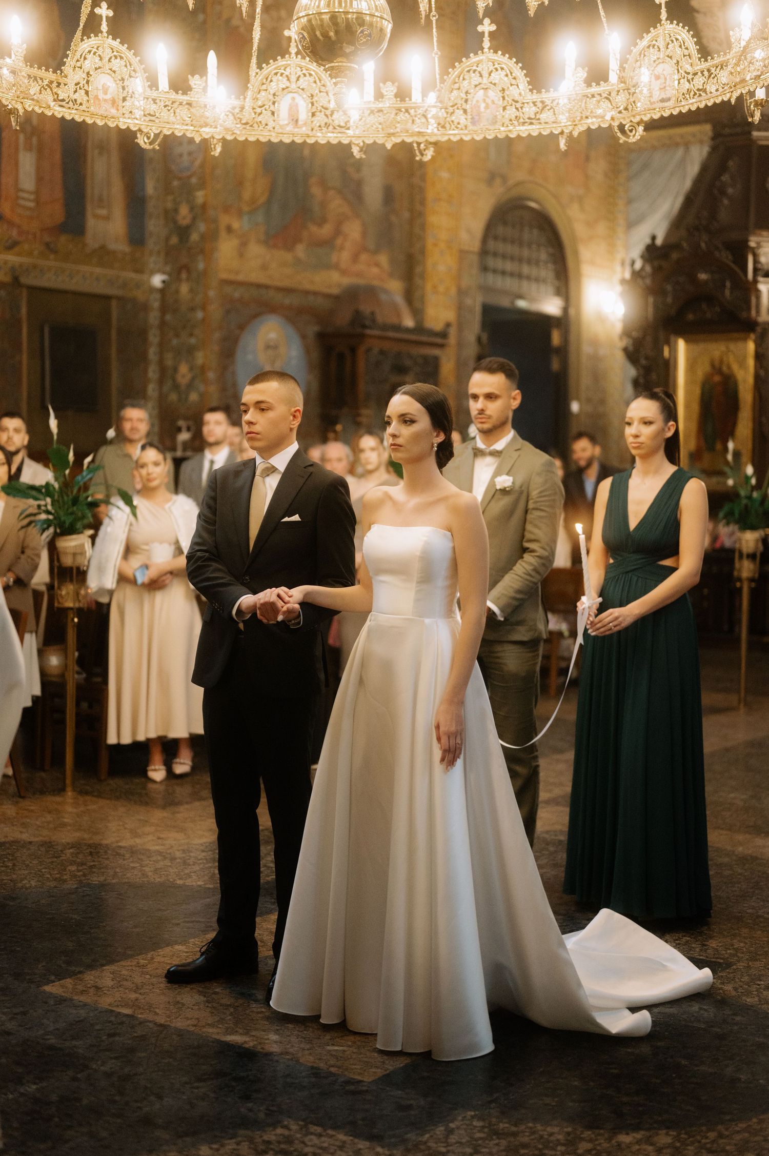 Elegant wedding ceremony in an ornate church with crystal chandeliers and guests gathered in formal attire.