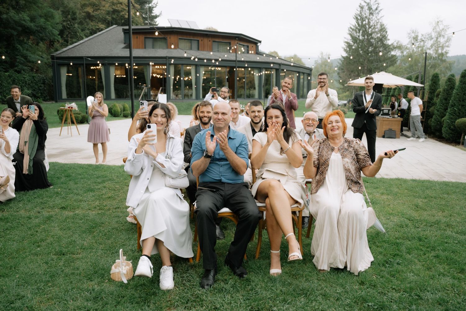 Wedding party relaxes on lawn chairs in outdoor garden setting during summer celebration.