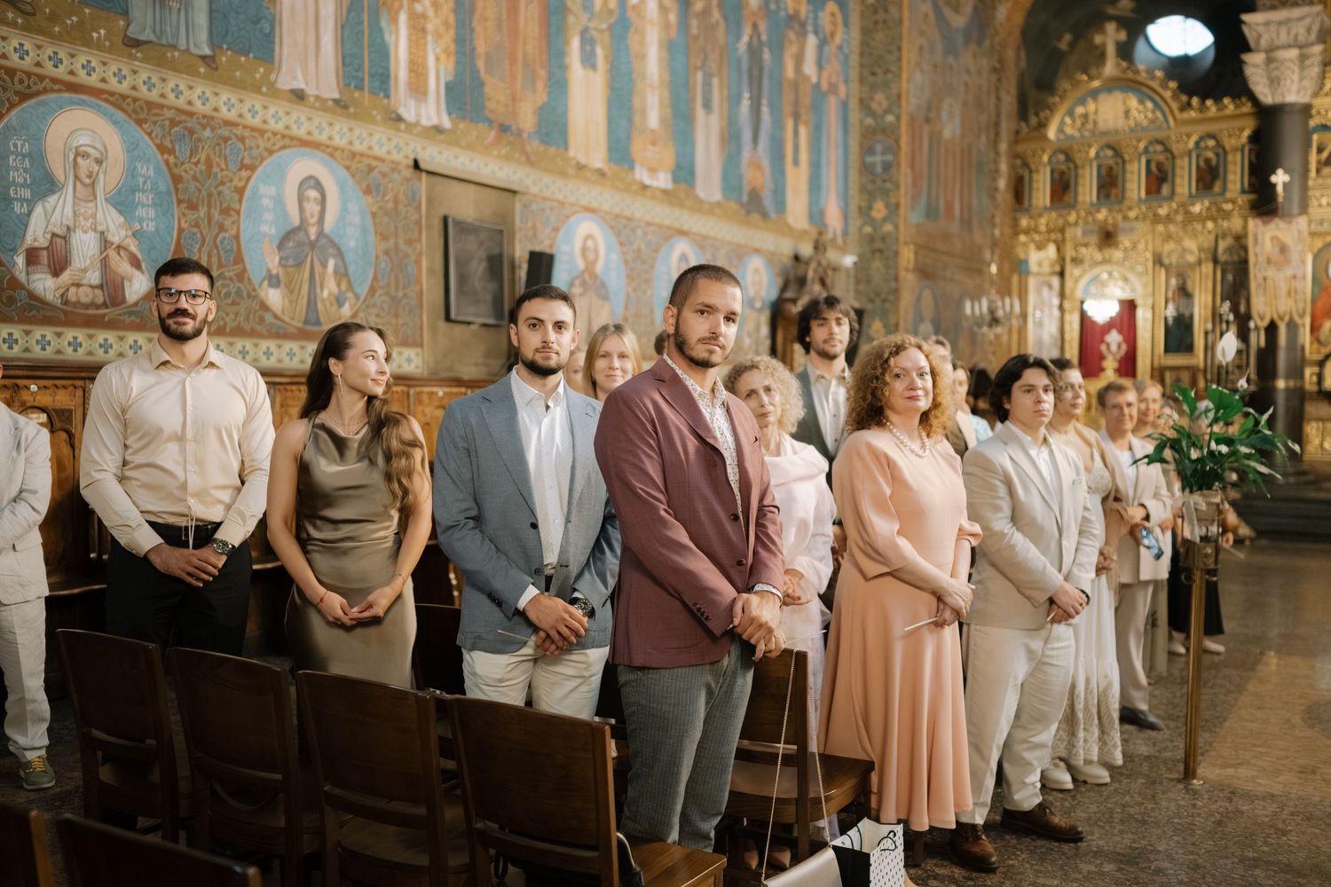 Wedding party poses in a line against an ornate church interior with golden frescoes and decorative architecture.