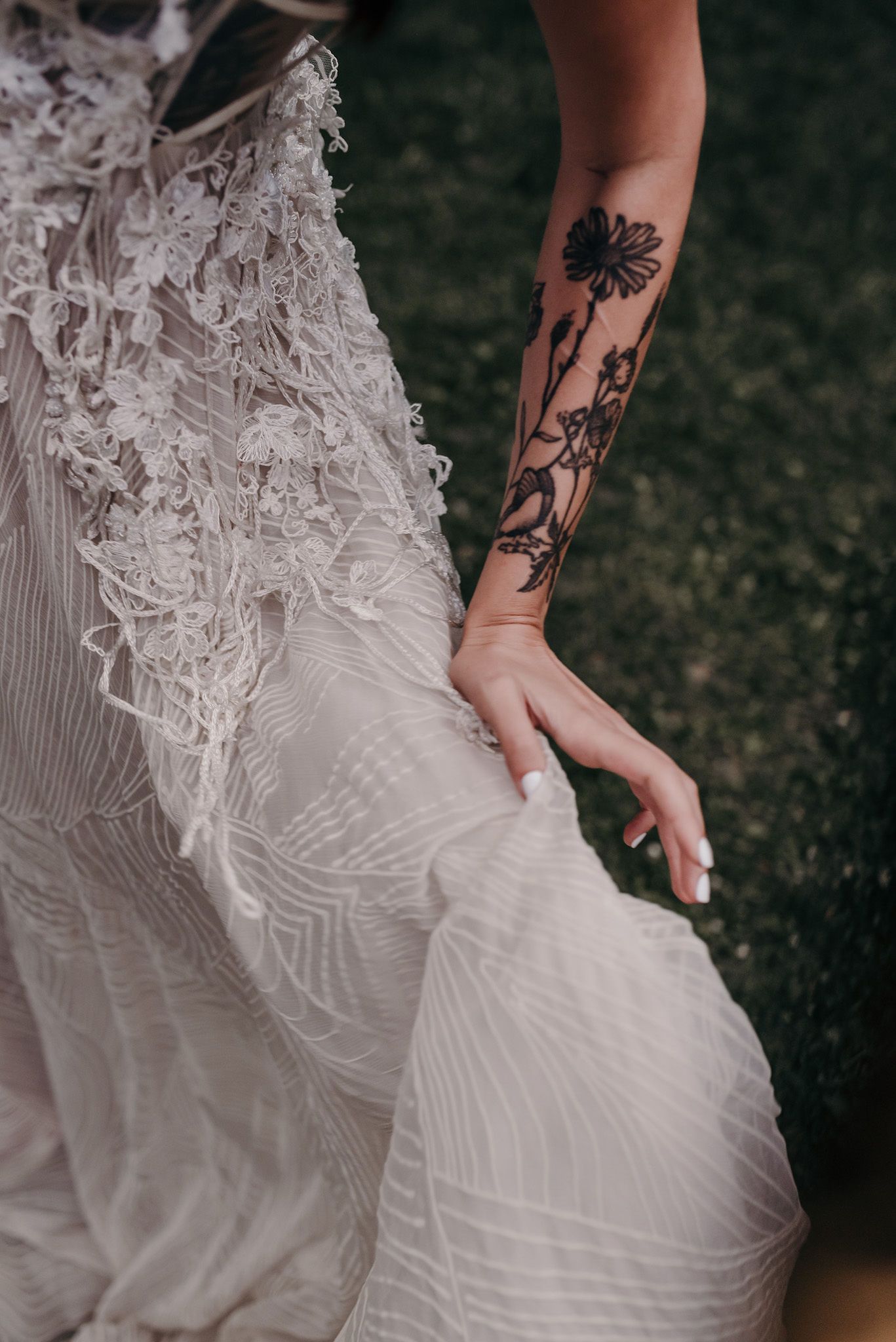 Close-up of a delicate lace wedding dress and an arm adorned with floral tattoo artwork.