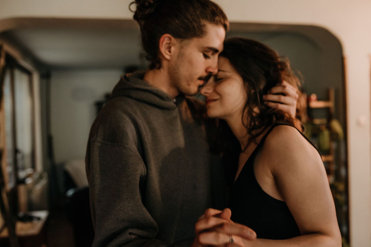 An intimate indoor photoshoot showing tender moments between a couple in warm lighting.