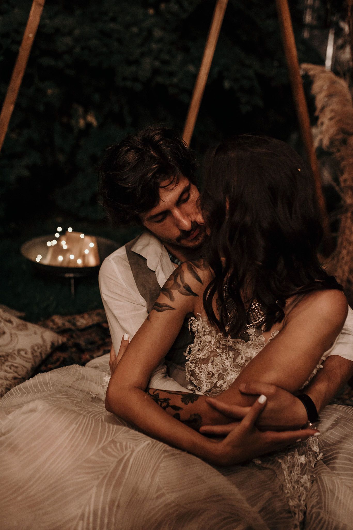 A romantic couple sharing intimate moments together on white bedding in a dimly lit setting.