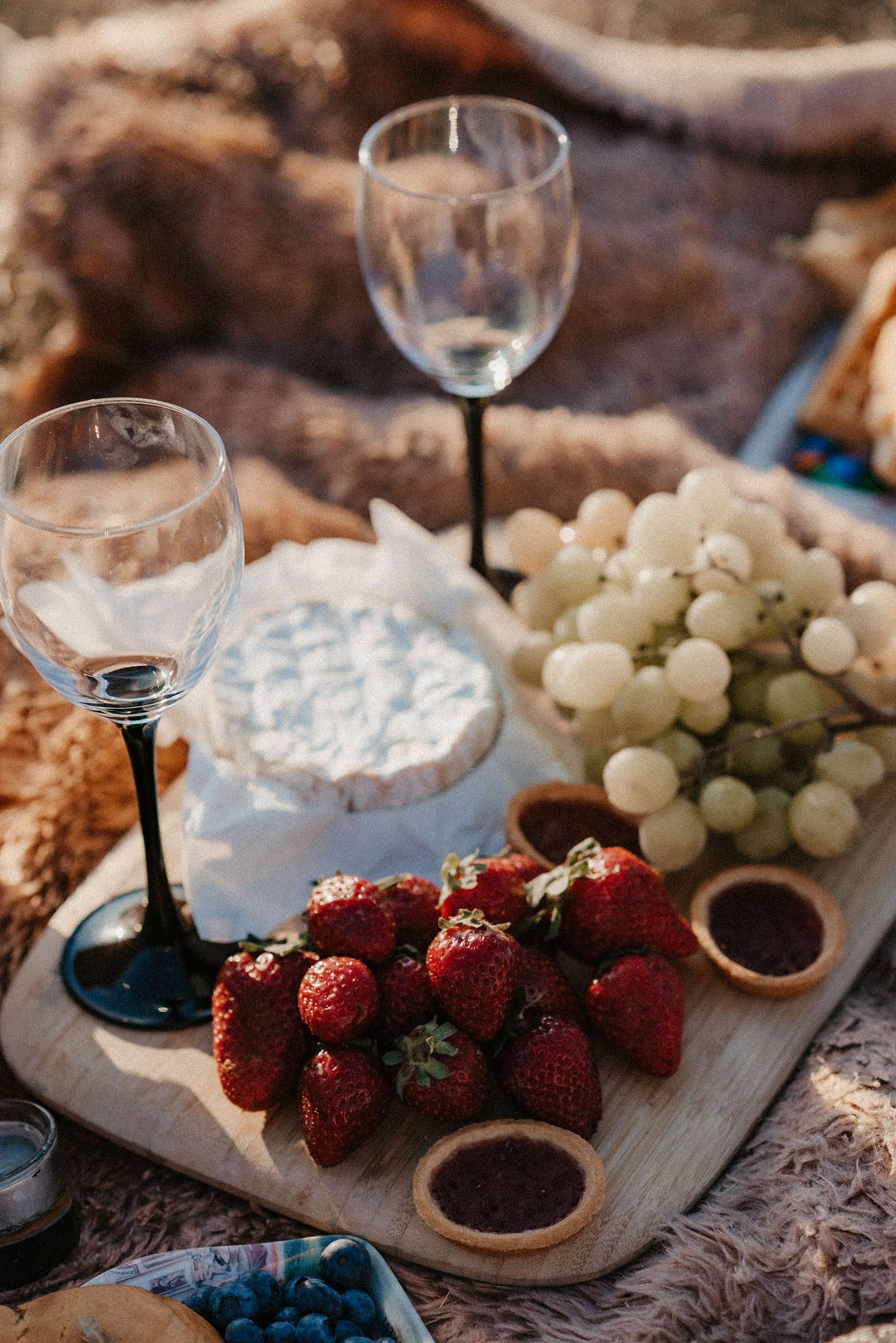 Fresh strawberries, grapes, and cheese arranged on a wooden serving board with wine glasses.