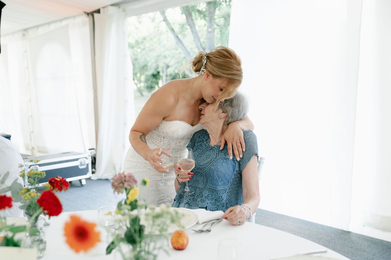 Wedding reception table settings with floral centerpieces and white linens under a tent.