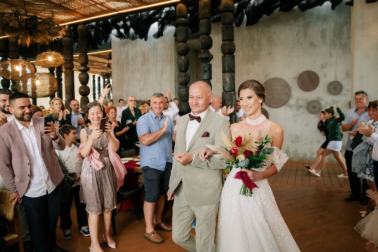 Wedding guests form an aisle in an industrial venue with exposed ceiling and concrete walls.