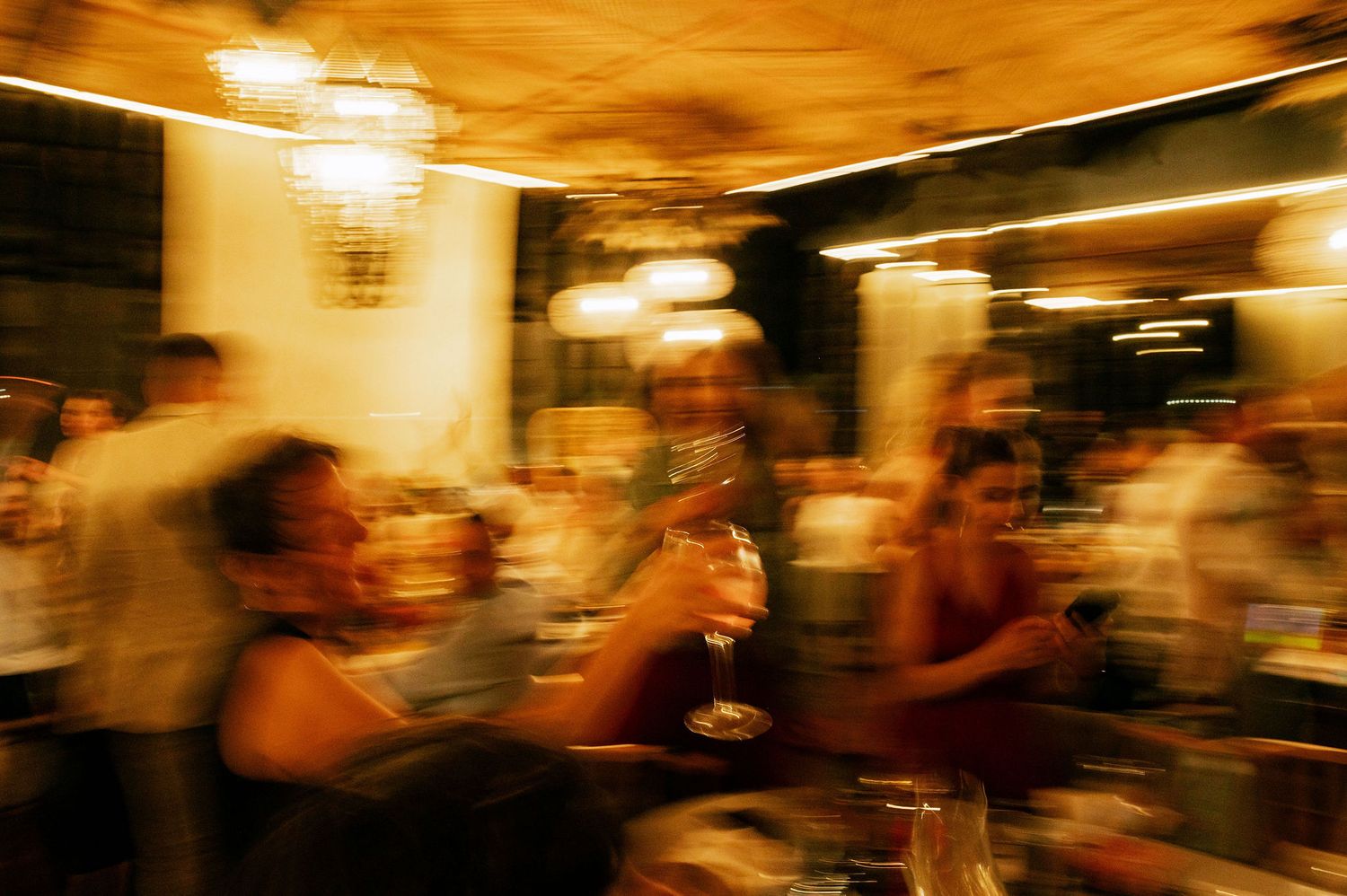 Motion-blurred scene of party guests dancing and celebrating in a warmly lit venue.