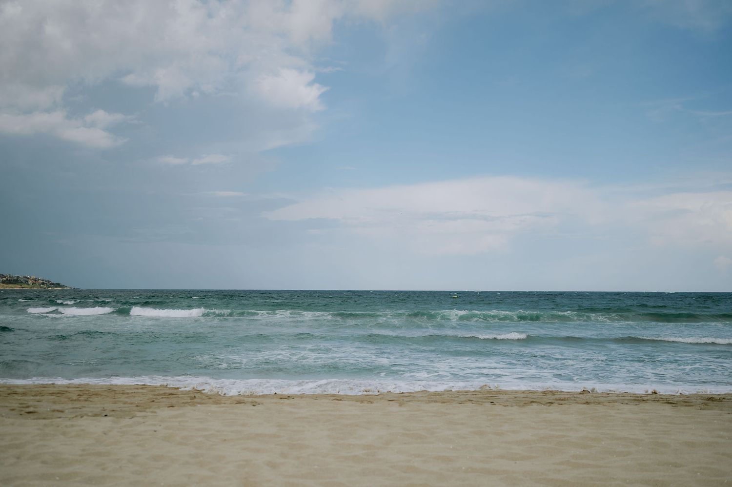 Scenic beach landscape with rolling waves and sandy shore under blue skies.