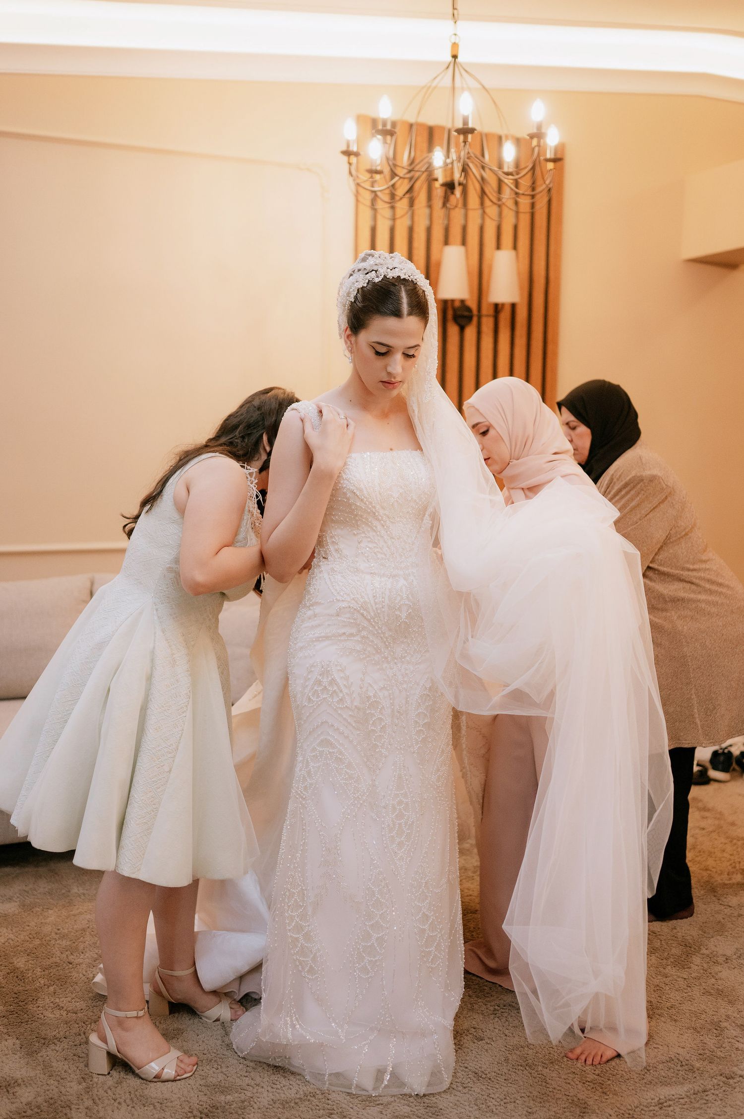 Helpers adjust the layers of a stunning white wedding gown during bridal preparations.