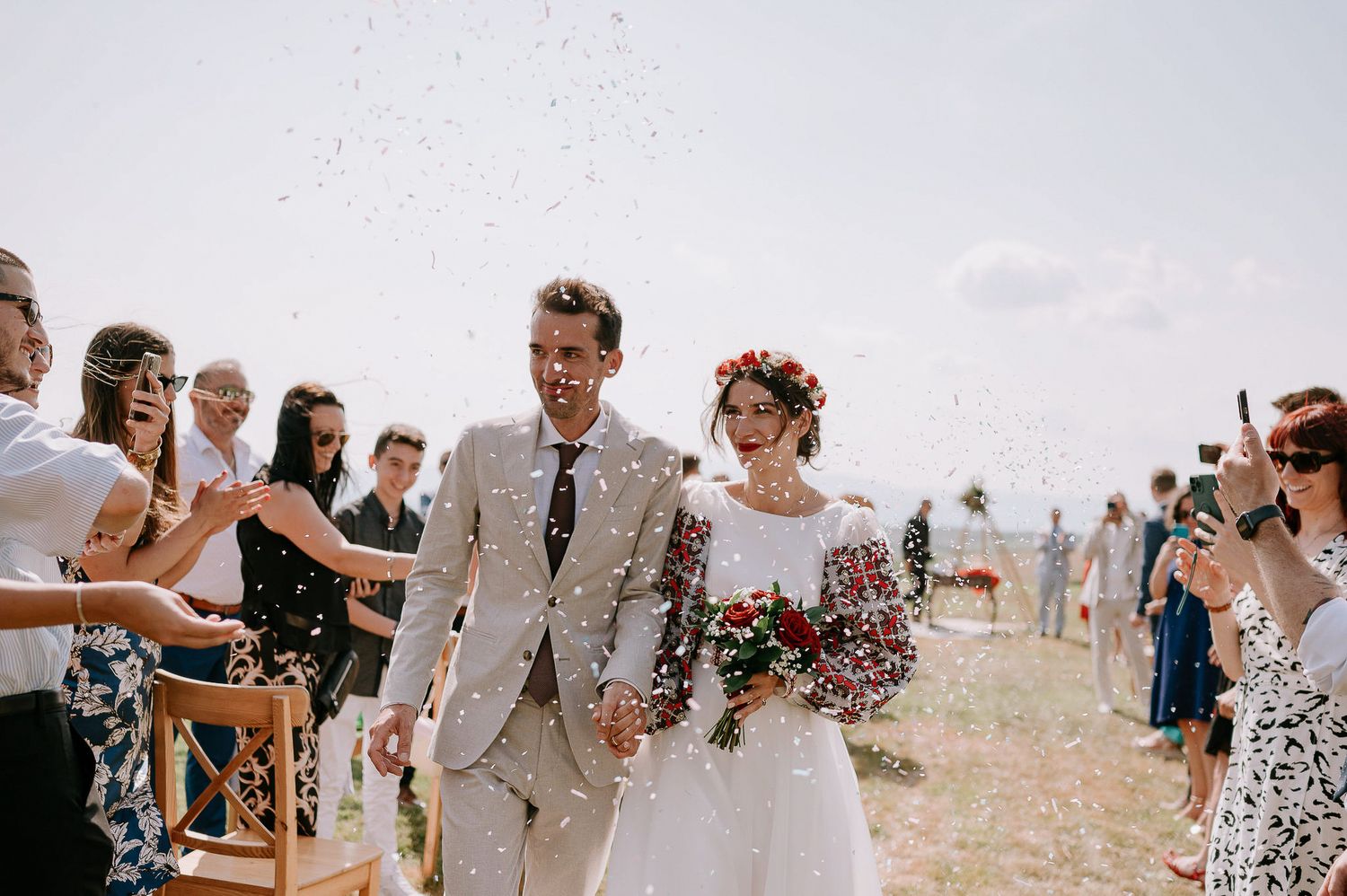 Newlyweds walking through confetti during their outdoor wedding recessional with guests celebrating.