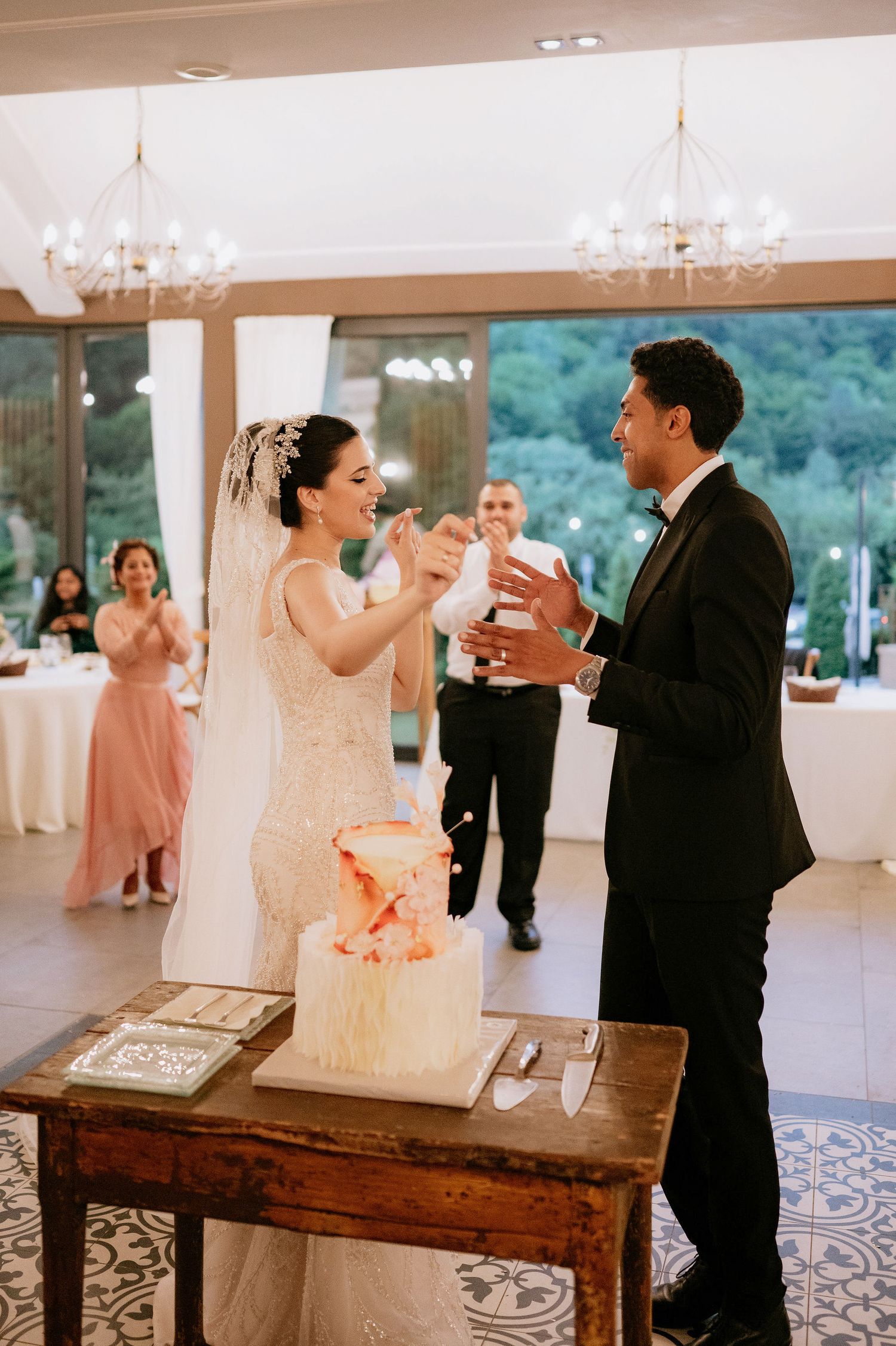 Wedding couple shares a playful cake-cutting moment at their reception by a rustic wooden table.