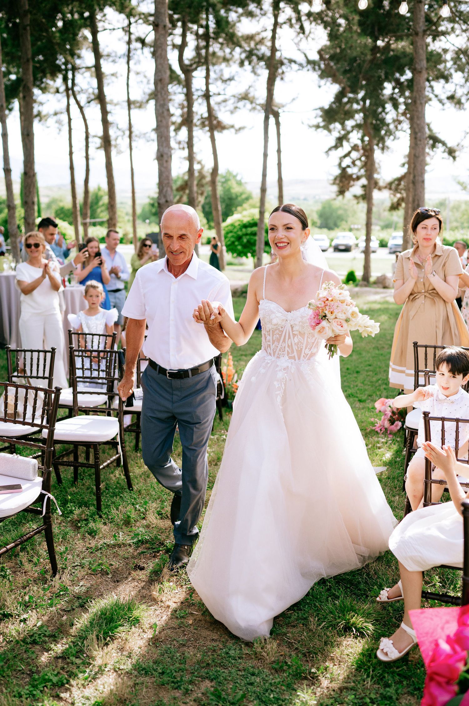 Joyful wedding celebration with guests and wedding party in a sunlit forest setting.