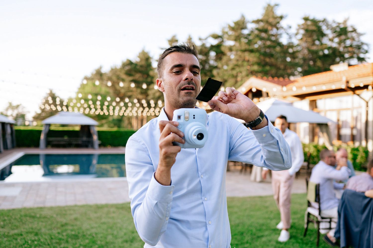 Wedding guests in formal attire celebrate outdoors during evening reception.