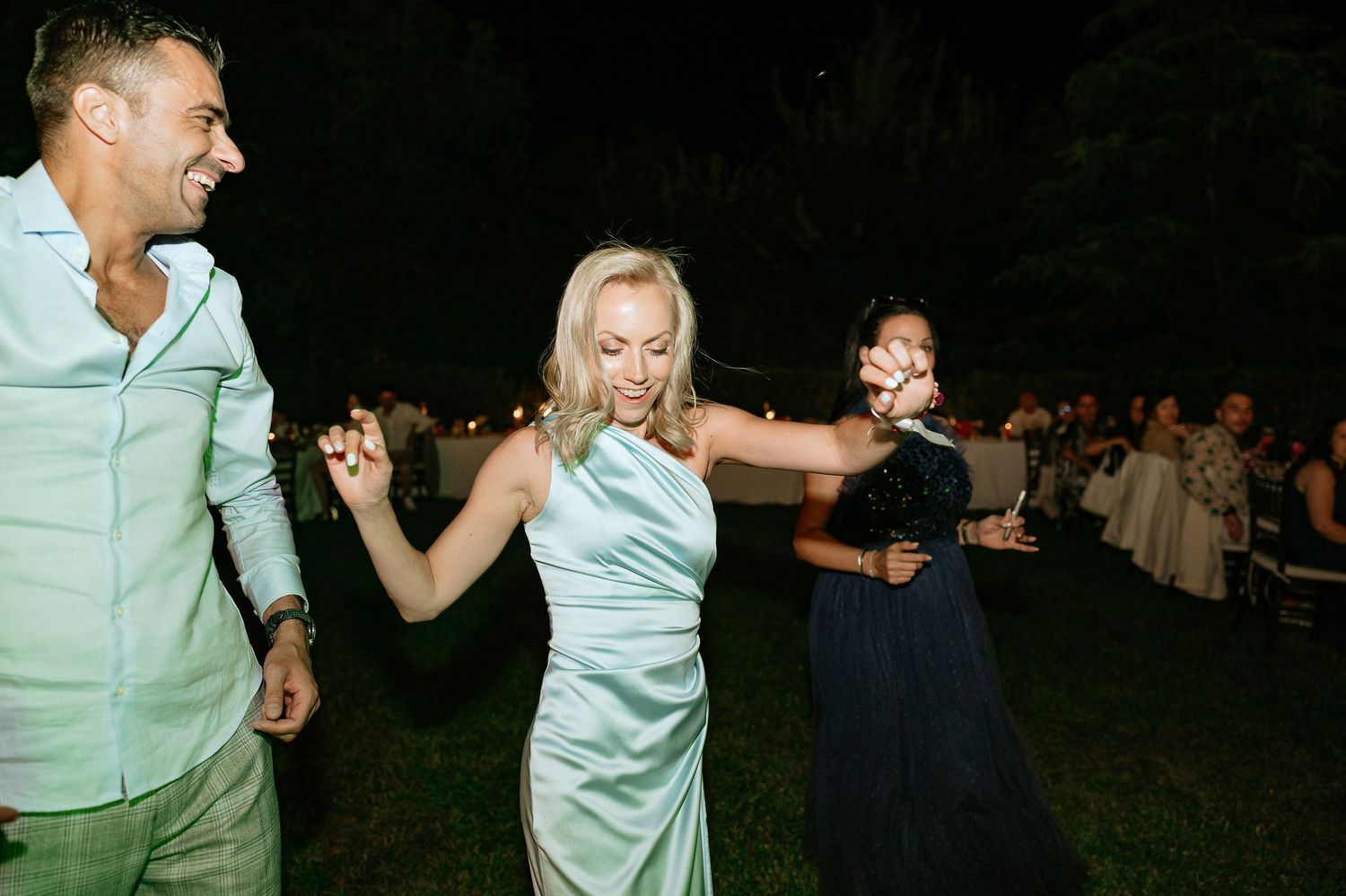 Wedding guests dancing enthusiastically at outdoor nighttime celebration.