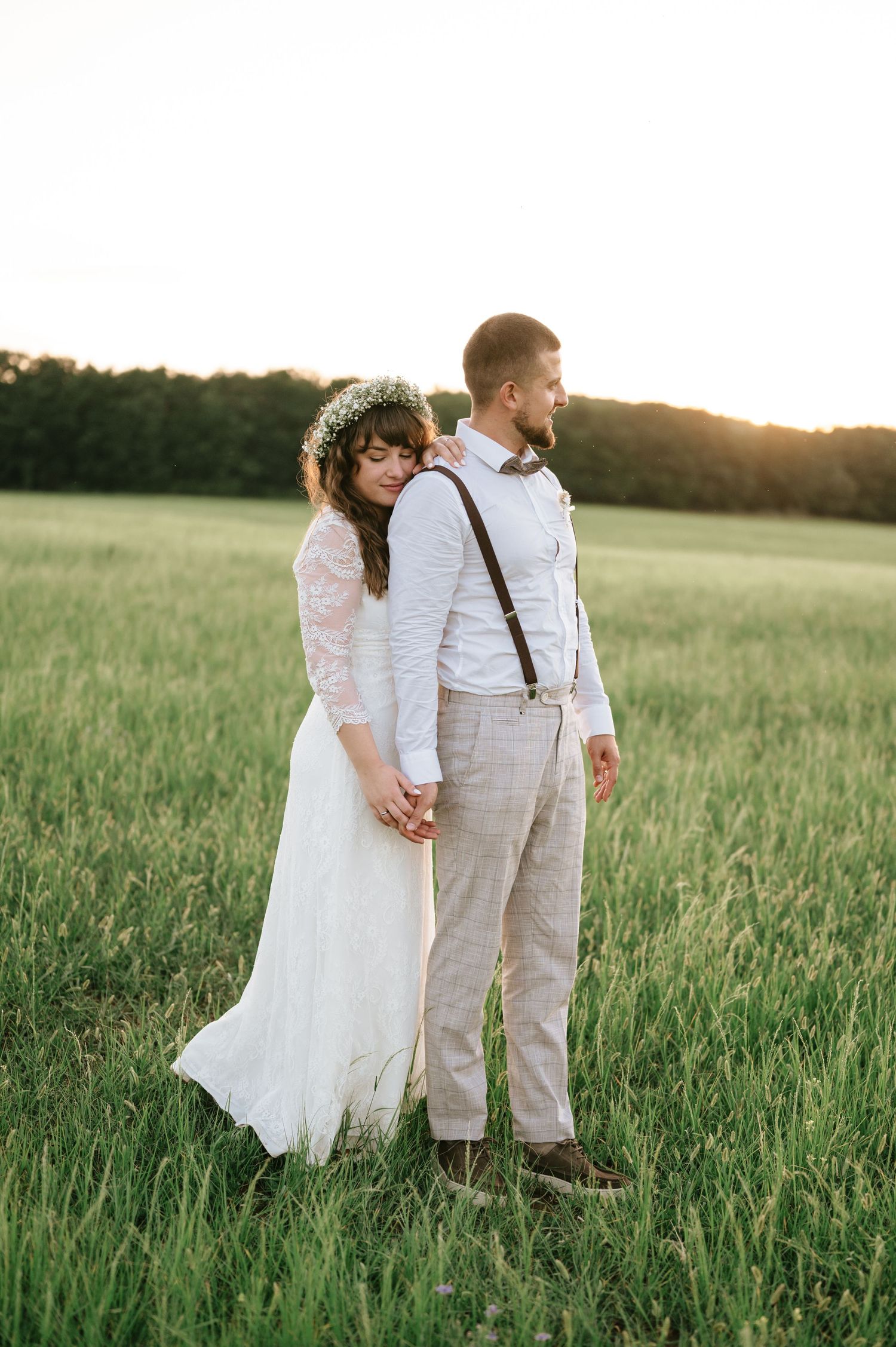A couple shares intimate moments in a sunlit field wearing wedding attire.
