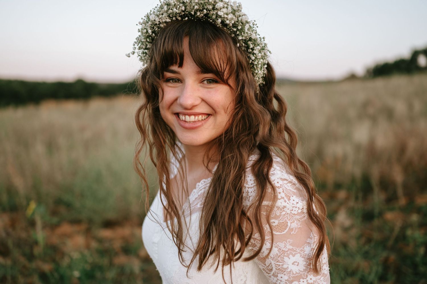 Portrait of bride wearing baby's breath flower crown and lace dress in natural outdoor setting.
