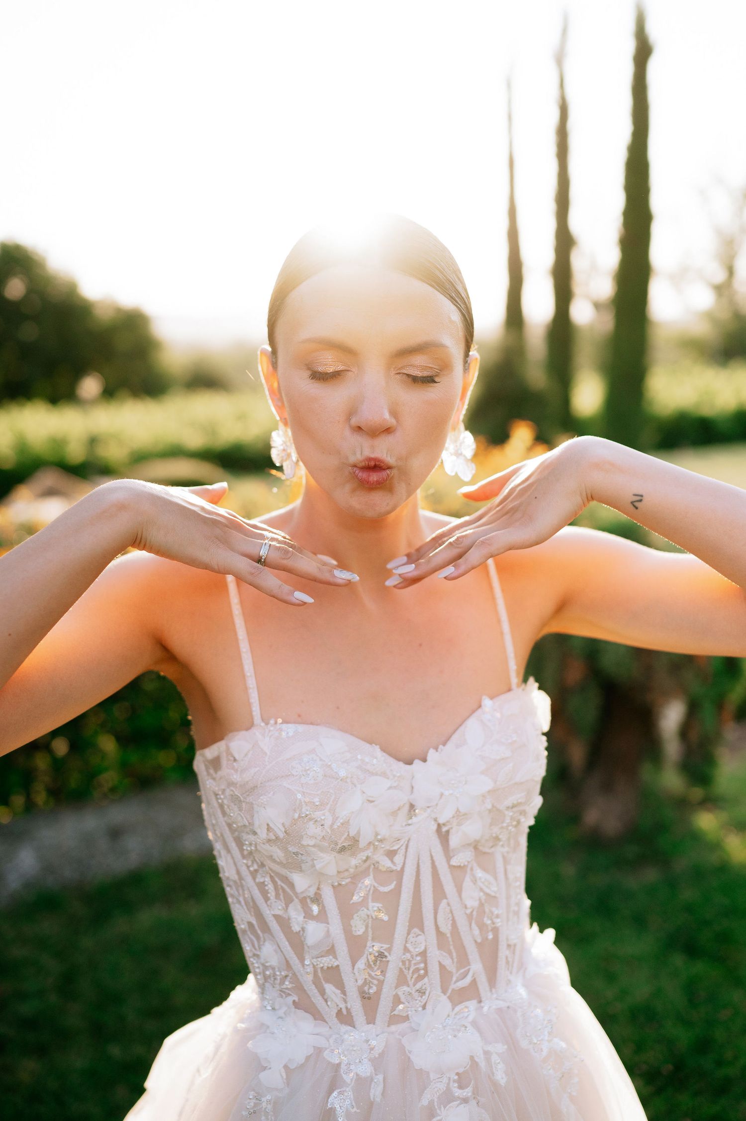 Close-up of bride in lace bodice gown with arms outstretched in golden sunlight.