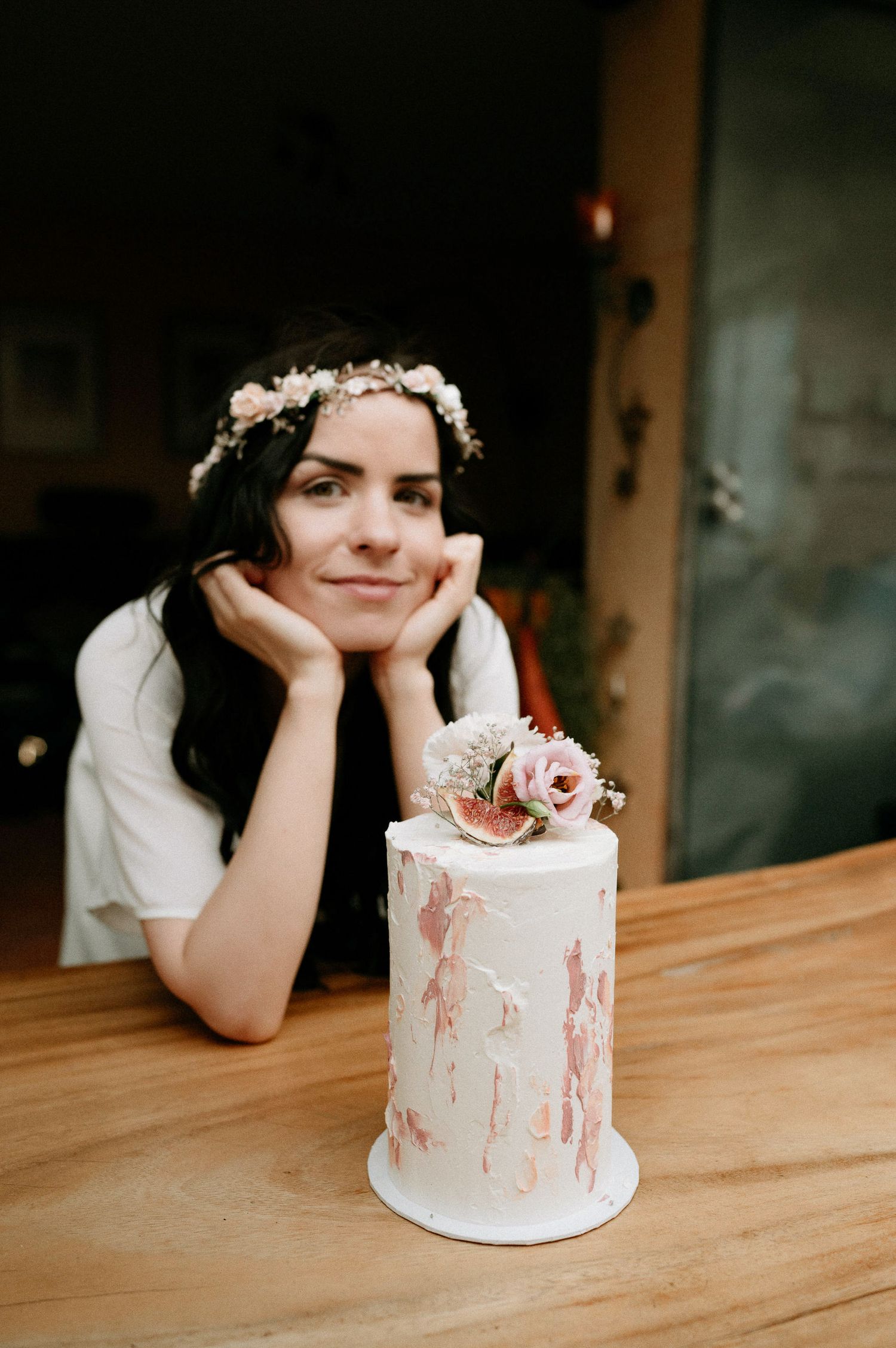 Person rests head on hands while admiring a small white wedding cake with floral decorations.