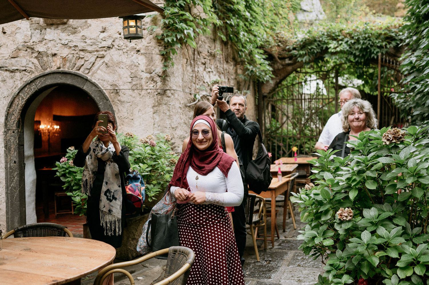 People gather in a charming garden courtyard with stone walls and climbing vines.