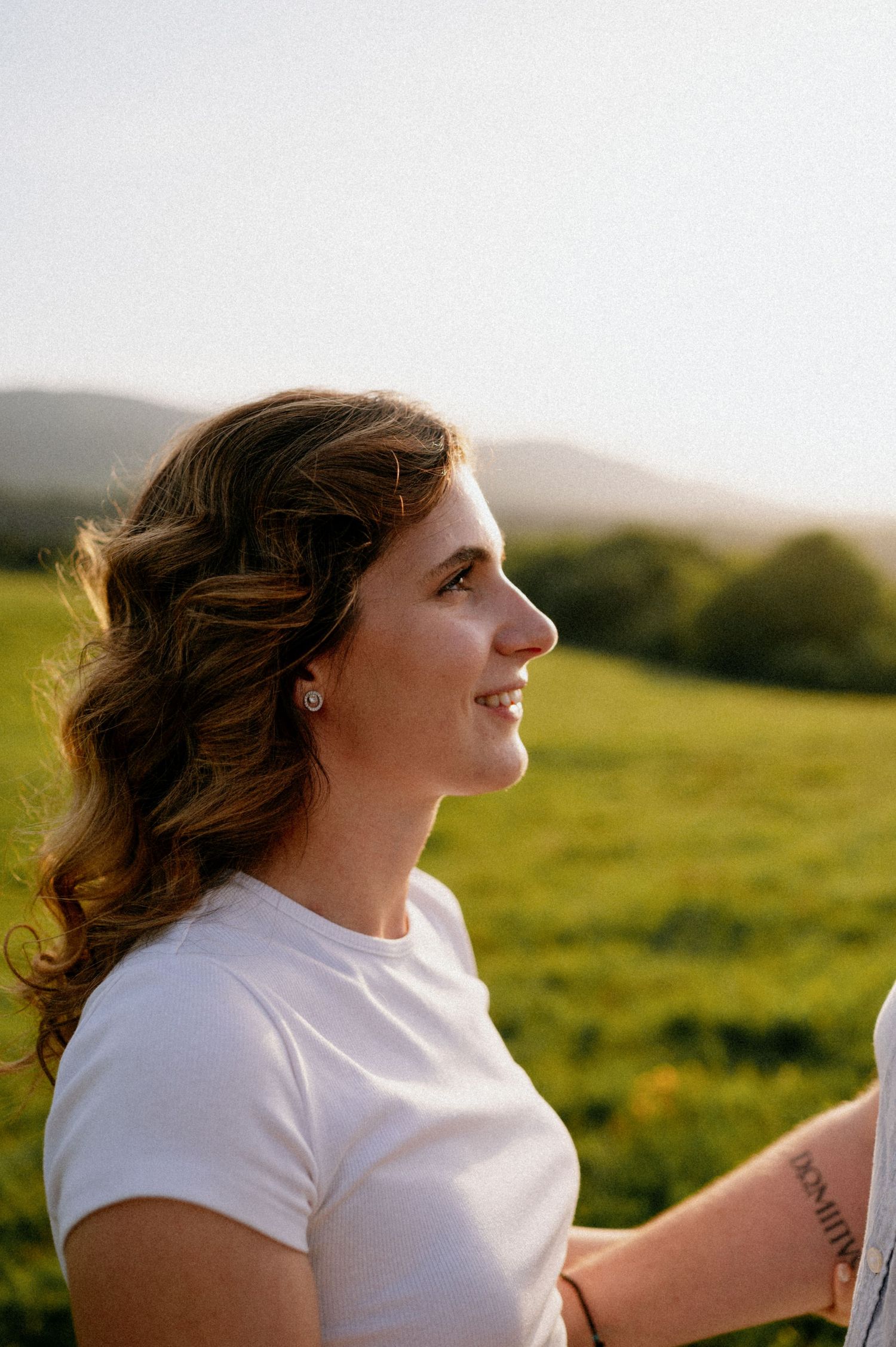 A person in a white shirt laughs joyfully while standing in a sunny meadow.