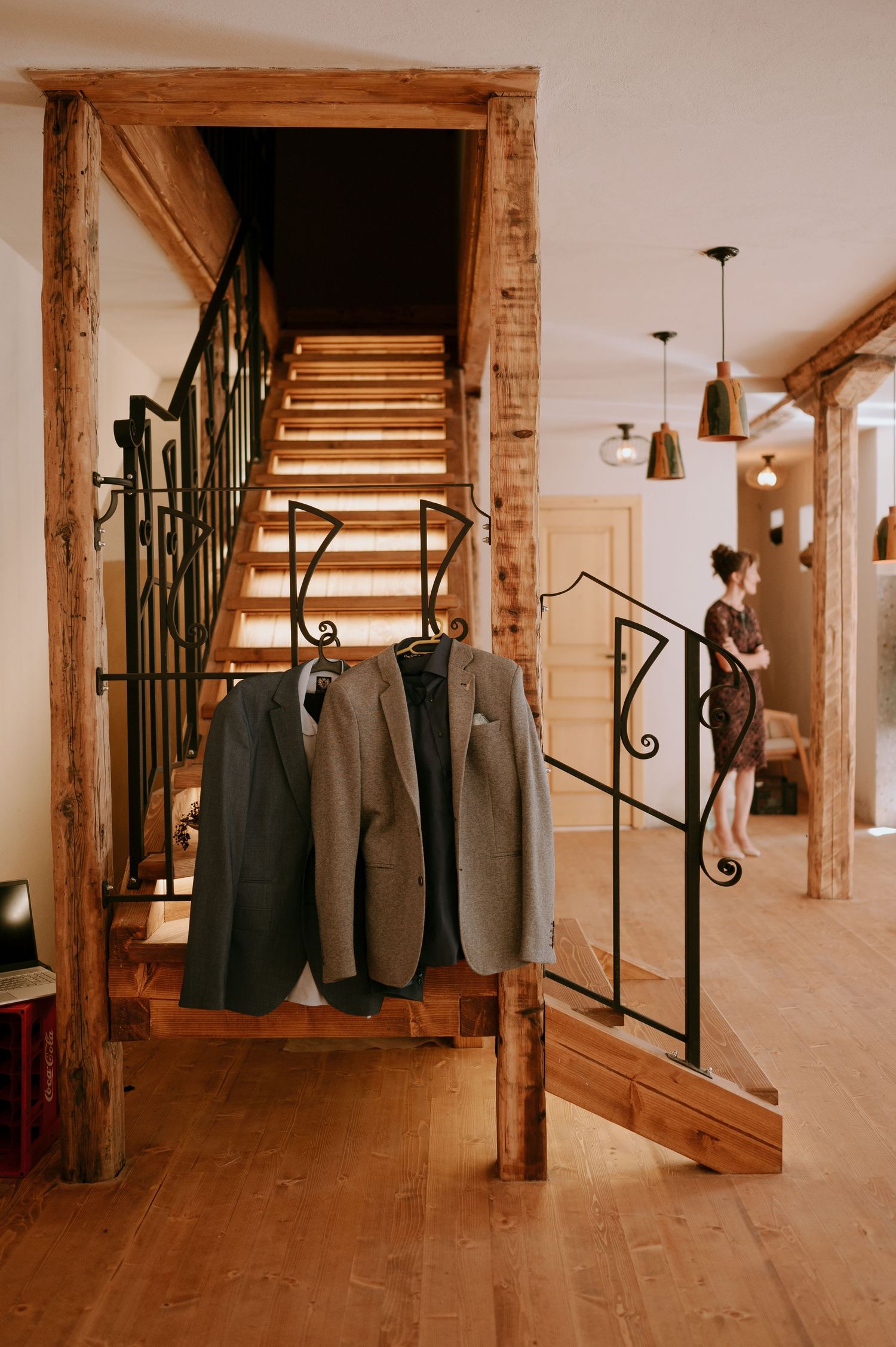 Grey suits hang on display in a rustic venue with wooden beams and staircase.
