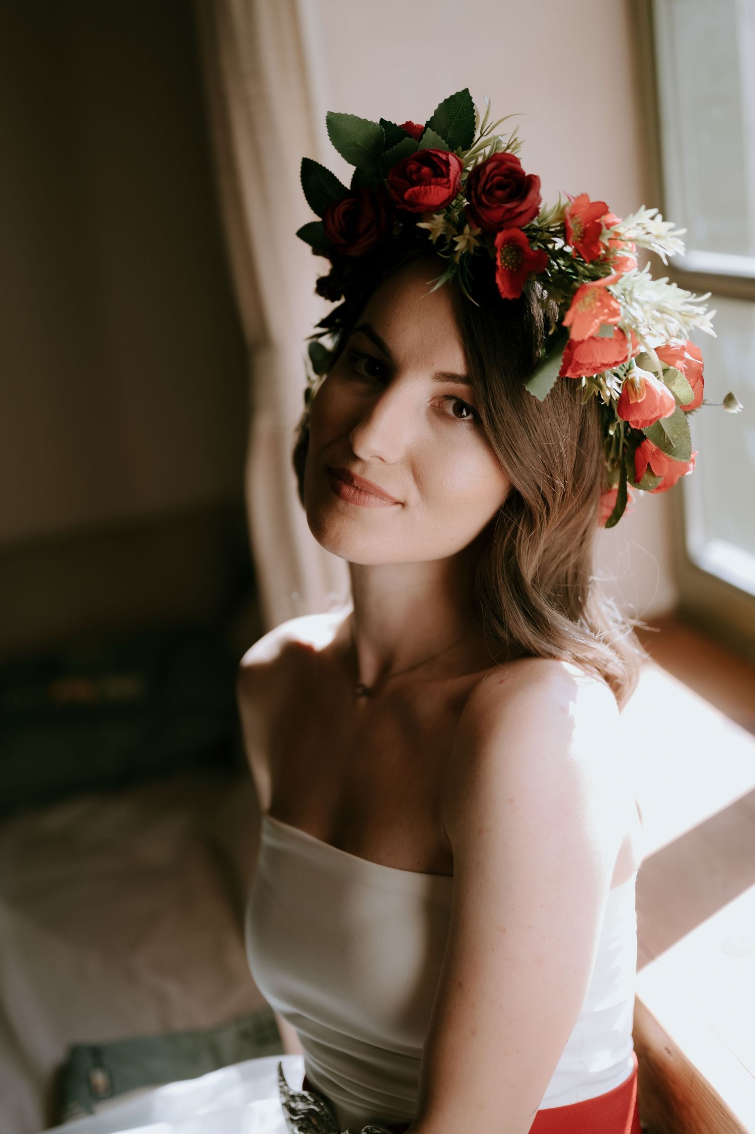A romantic bridal portrait featuring a floral crown with red roses against a soft natural light background.