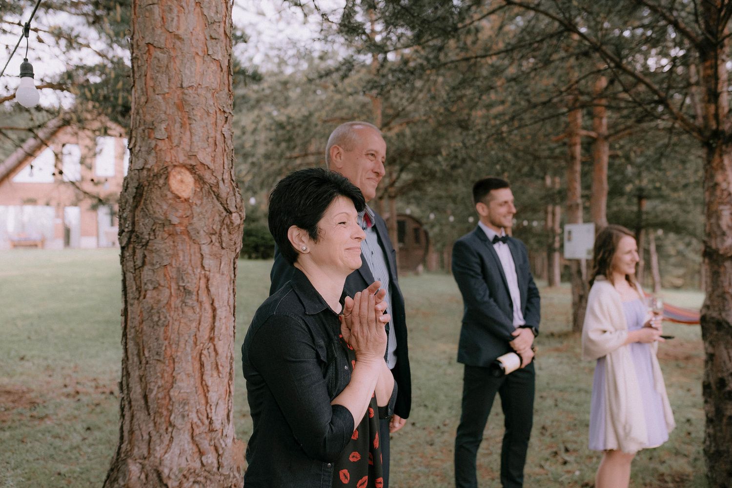 Wedding guests gather under tall pine trees for an intimate outdoor ceremony.