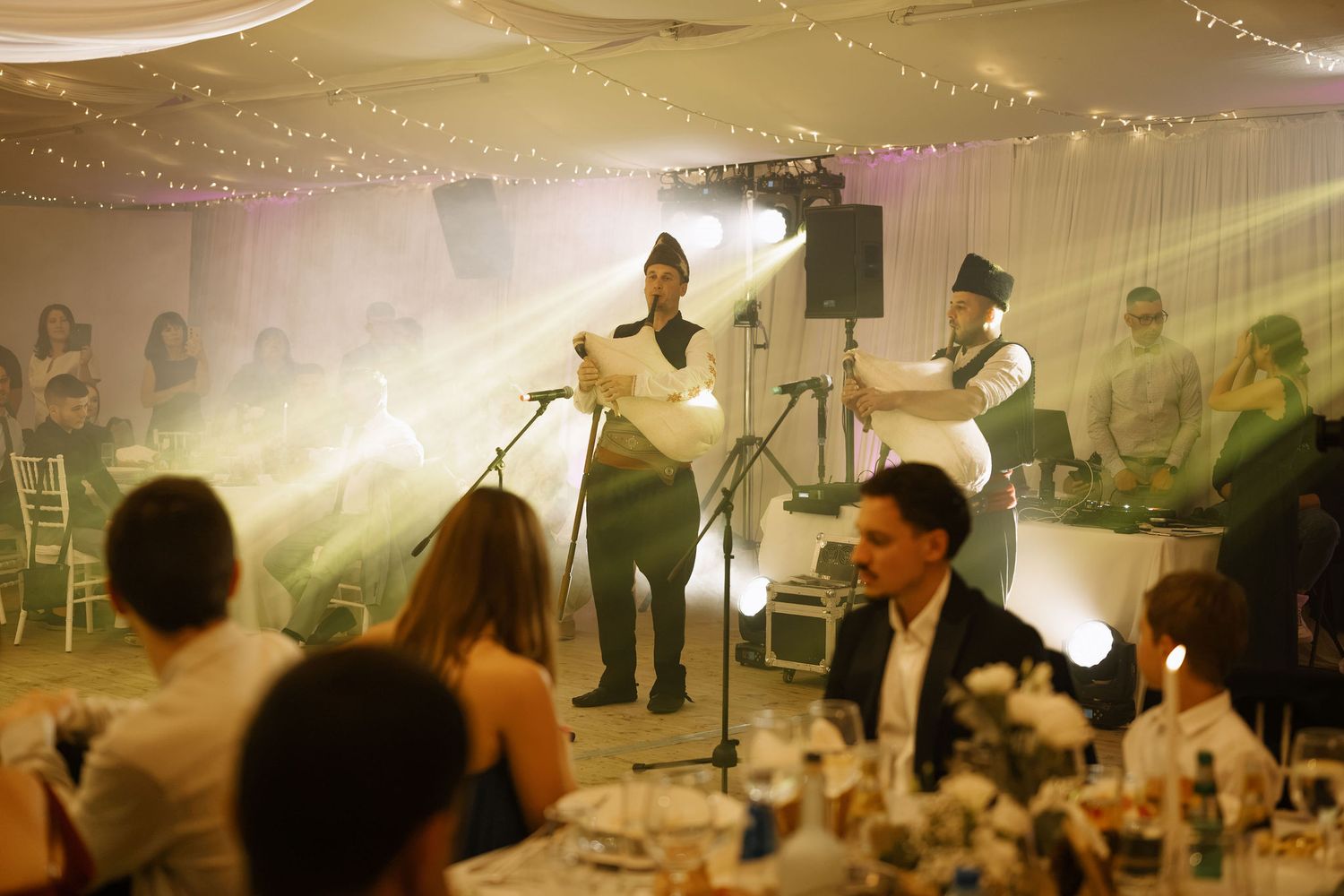 Live performers entertaining guests at an elegant wedding reception in a decorated tent venue with atmospheric lighting.