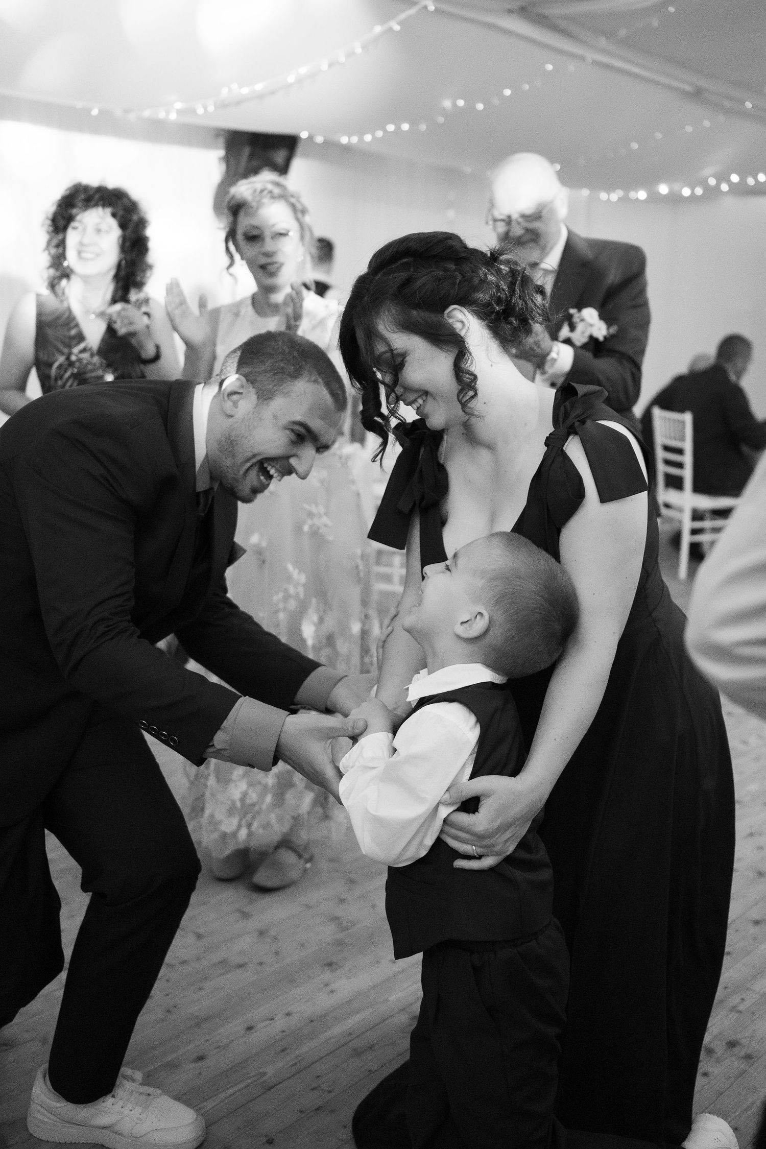 Black and white photo of a couple laughing with a young boy on a wedding dance floor.