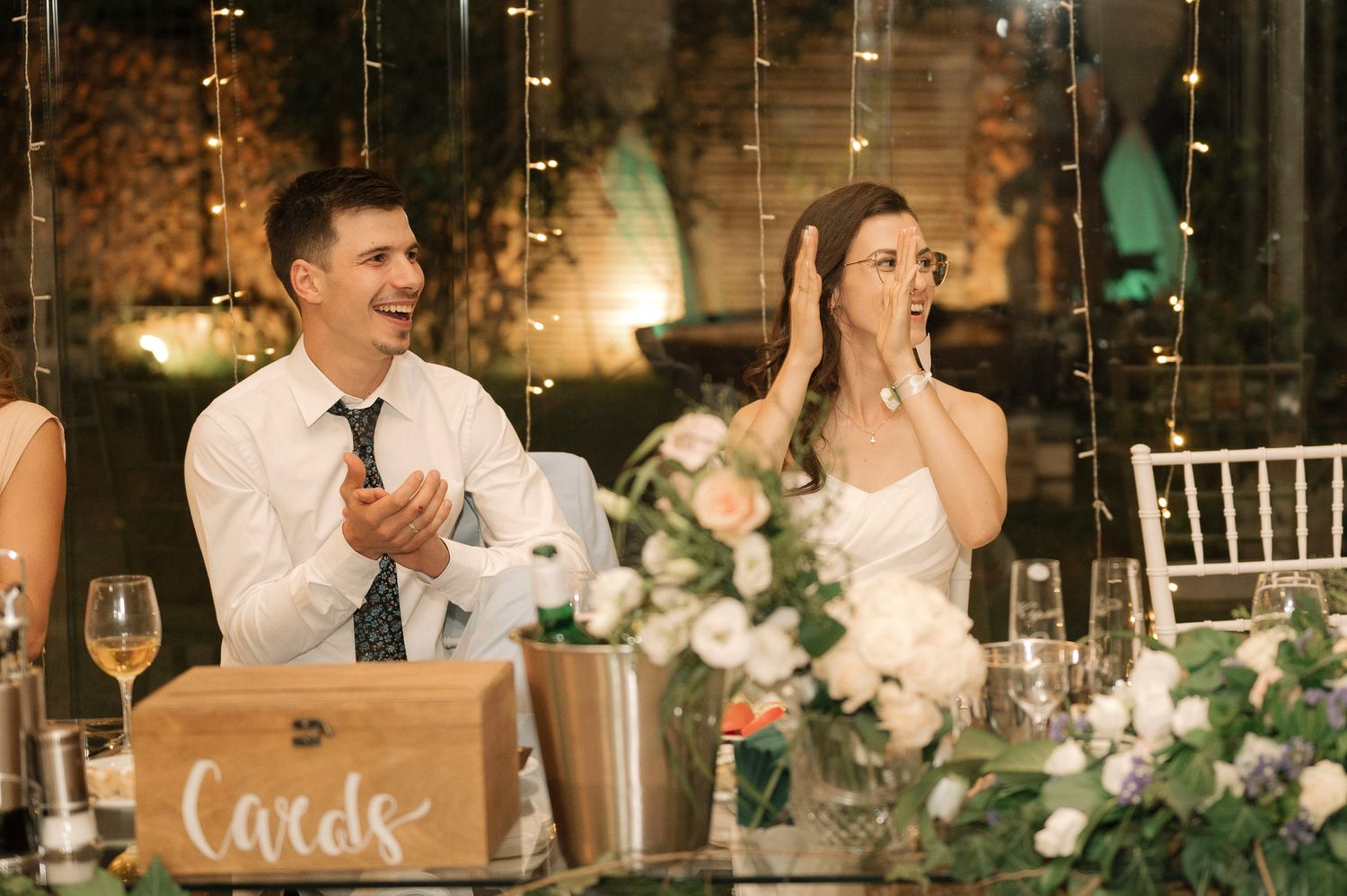 Couple reacts emotionally at an elegant wedding reception with floral centerpieces and candlelit decor.