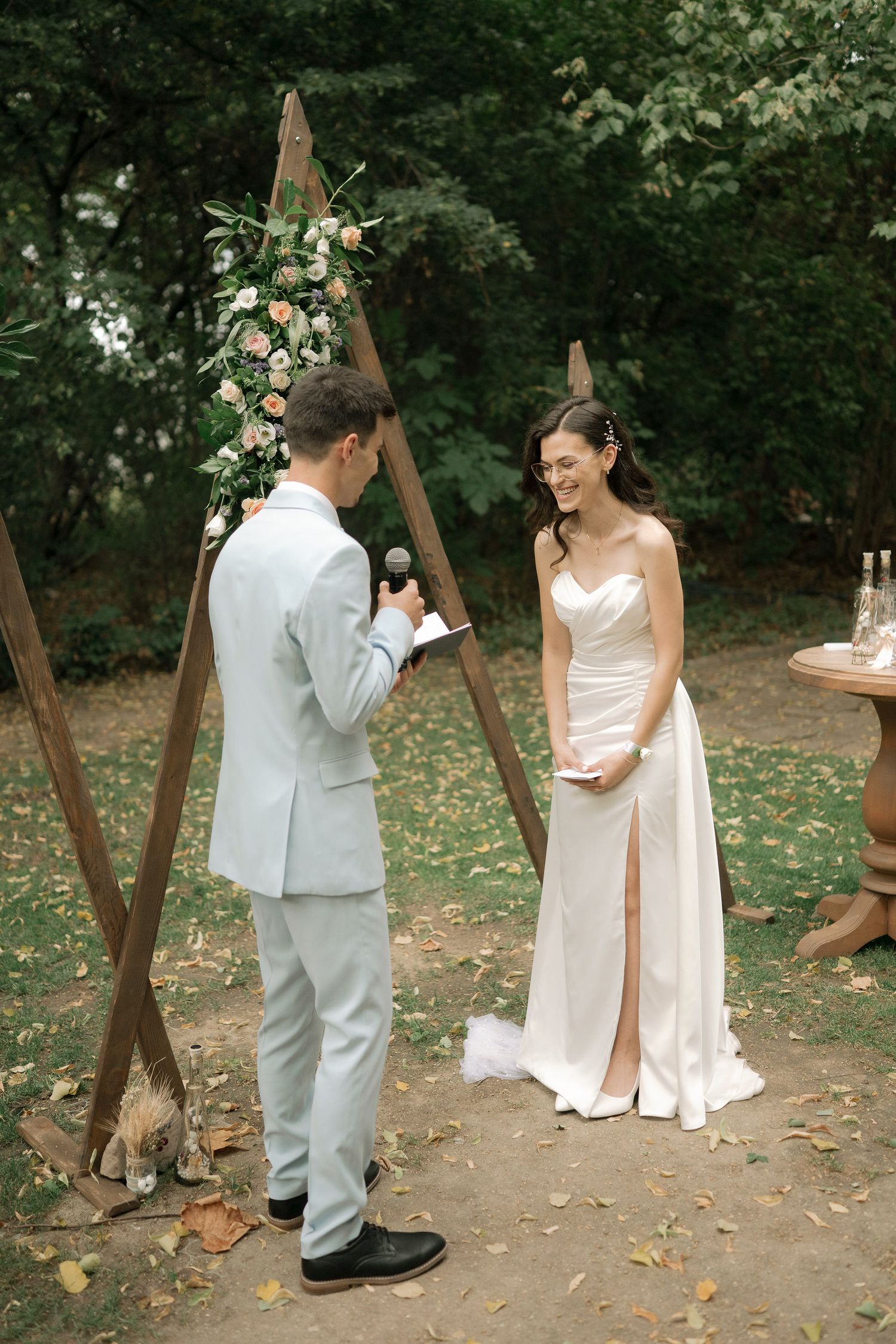 Couple shares a playful moment during their outdoor wedding photoshoot near rustic wooden posts in a wooded setting.