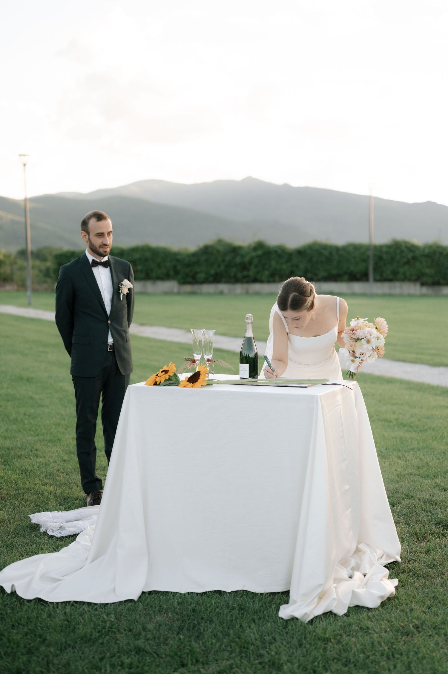 A couple at their outdoor wedding reception with a decorated sweetheart table against a mountain backdrop.
