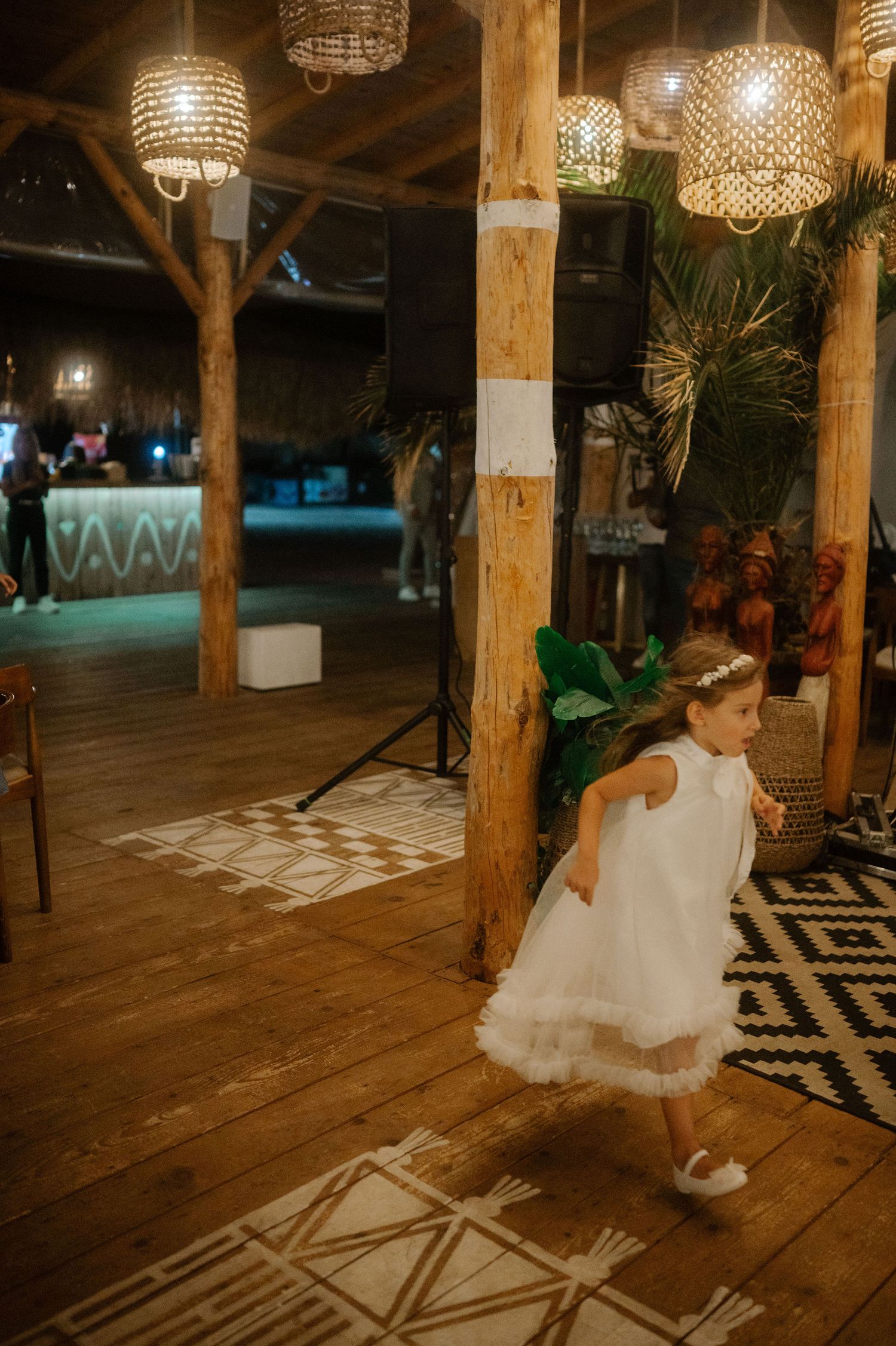 A flowing white wedding dress twirls on a rustic wooden dance floor under crystal chandeliers at an evening reception.