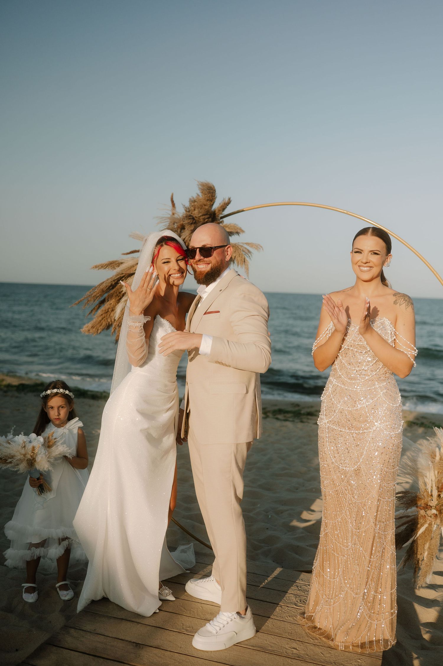 A beachside wedding celebration on a wooden deck with people in formal attire laughing and enjoying the ocean view.