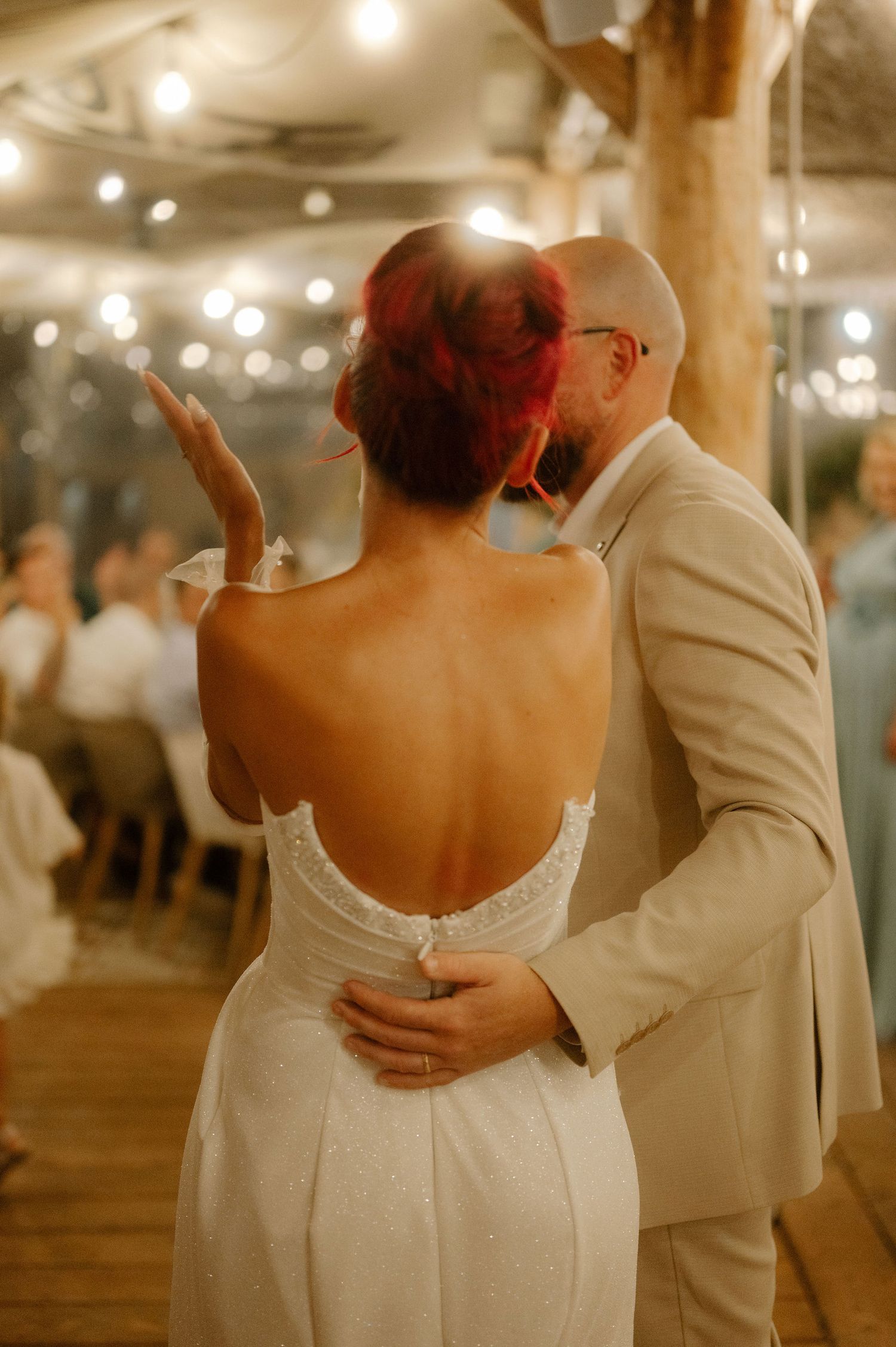 A couple in wedding attire dances together in an intimate moment on a warmly lit dance floor.