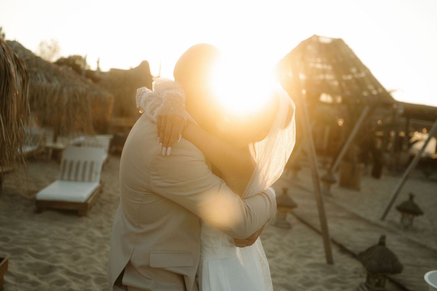 Silhouetted figures enjoy a romantic sunset moment on a beach with chairs and glowing golden light.