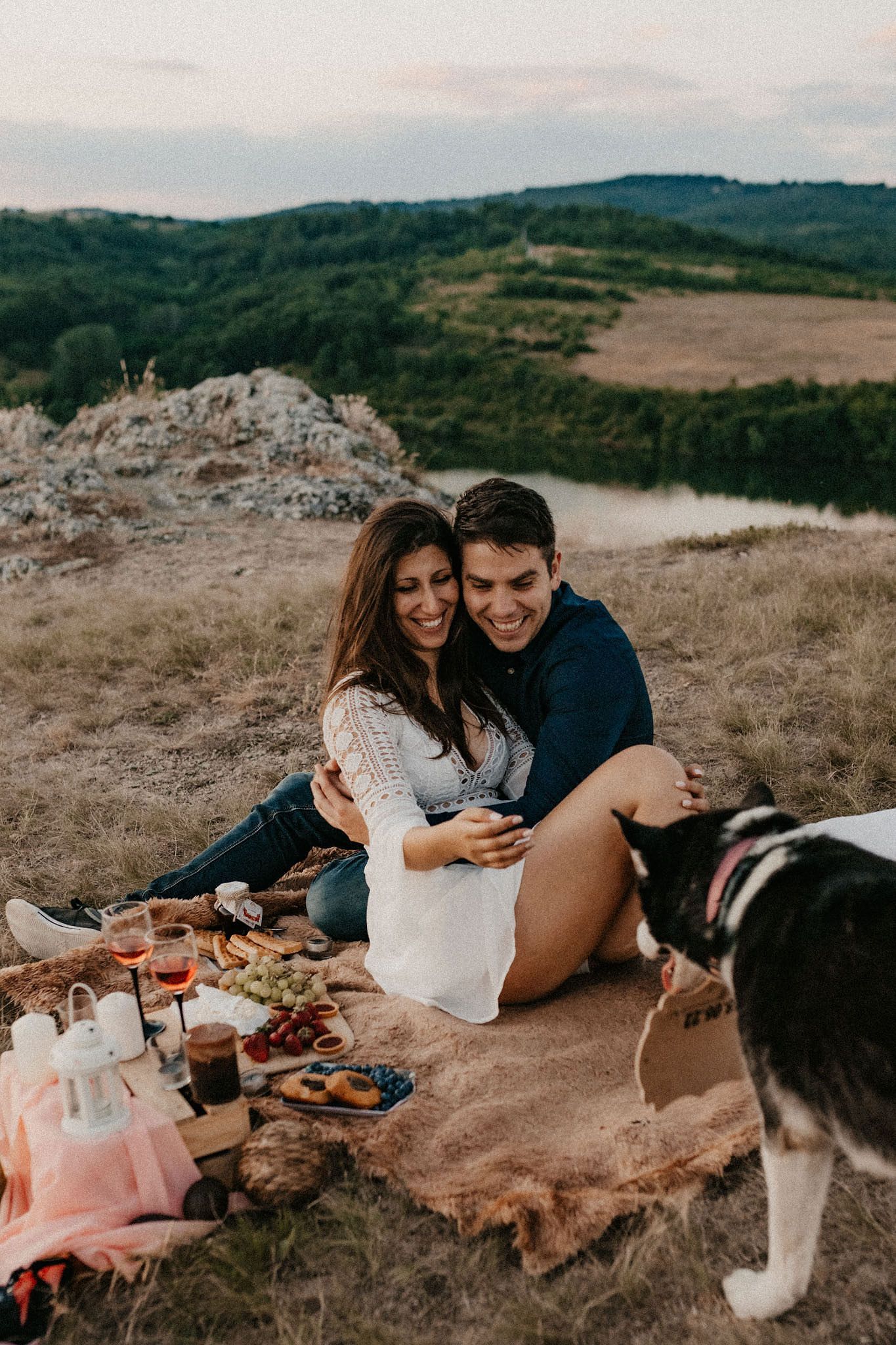 Romantic picnic setup on a hilltop with wine, snacks and a husky dog joining the couple.
