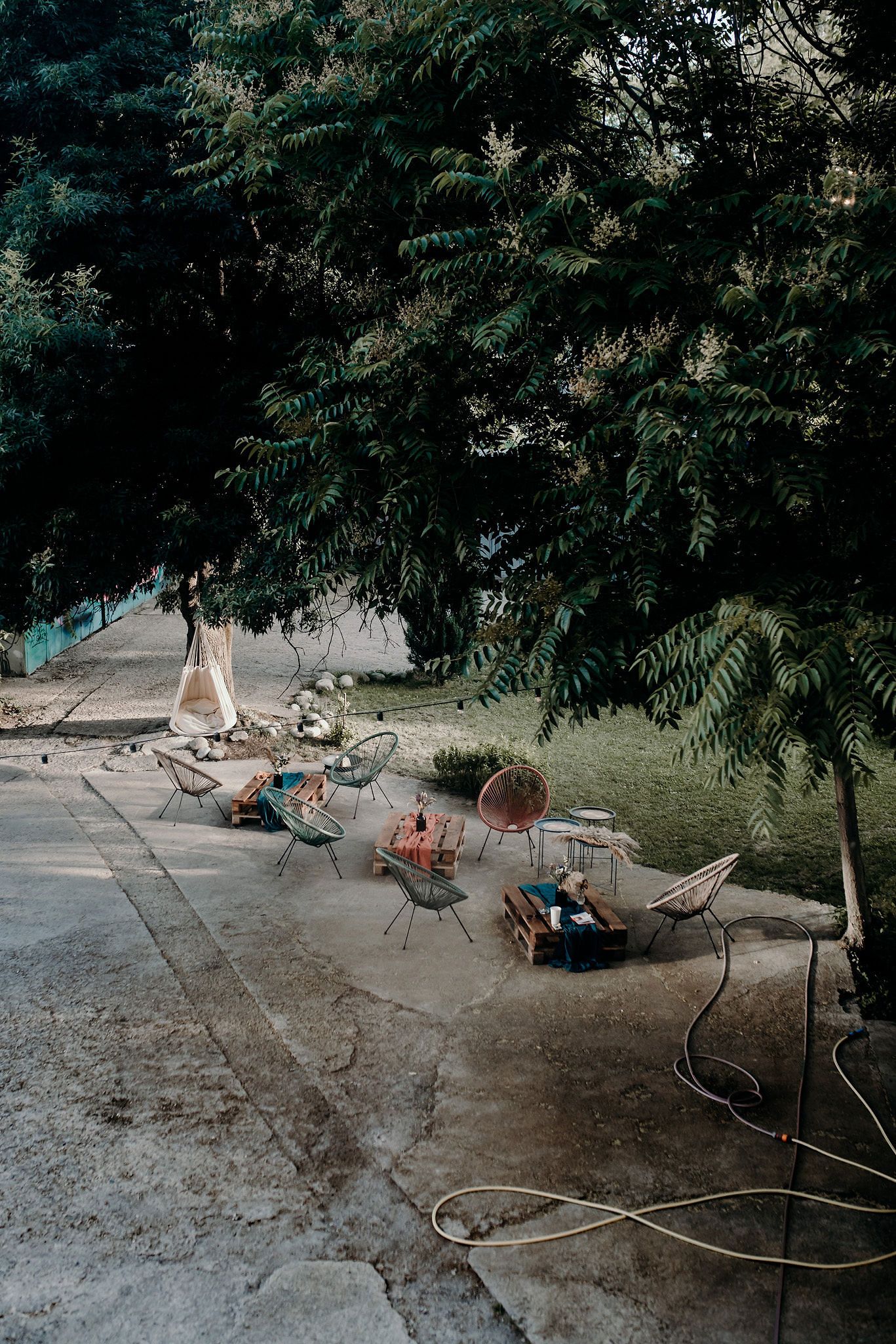 Outdoor seating area with scattered chairs under leafy trees.