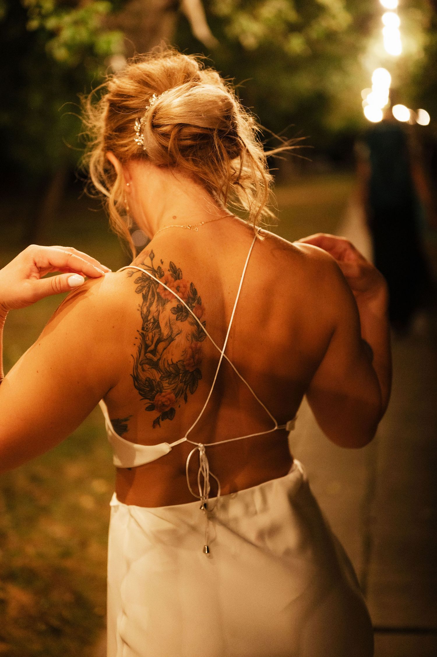 A close-up view of a bride's back showing an intricate floral tattoo and strappy white dress details.
