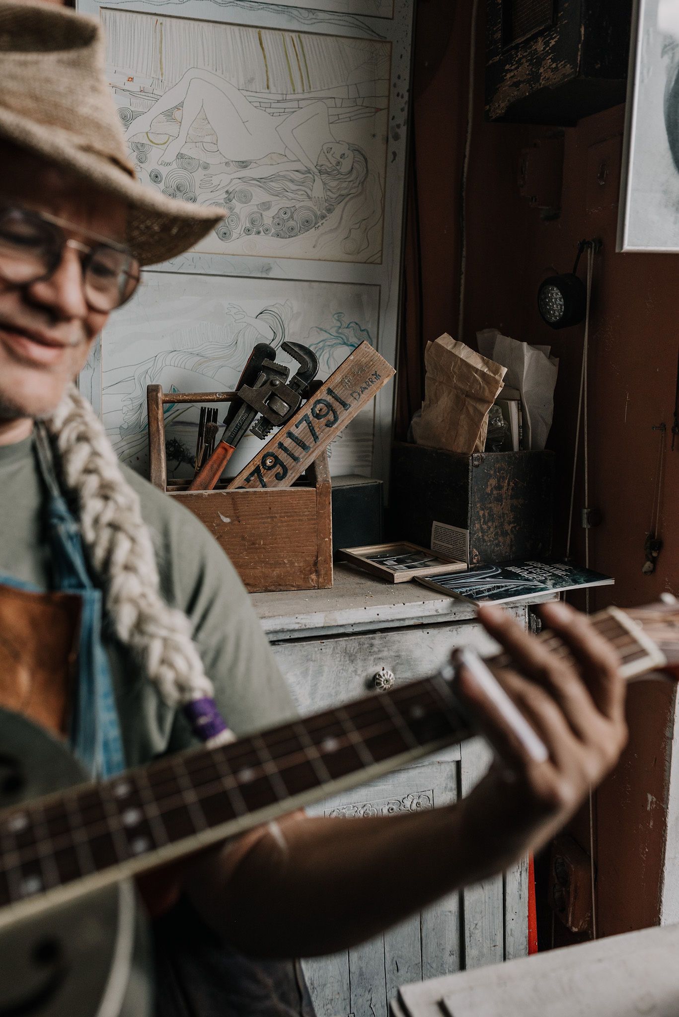 A musician plays acoustic guitar in a rustic indoor setting.