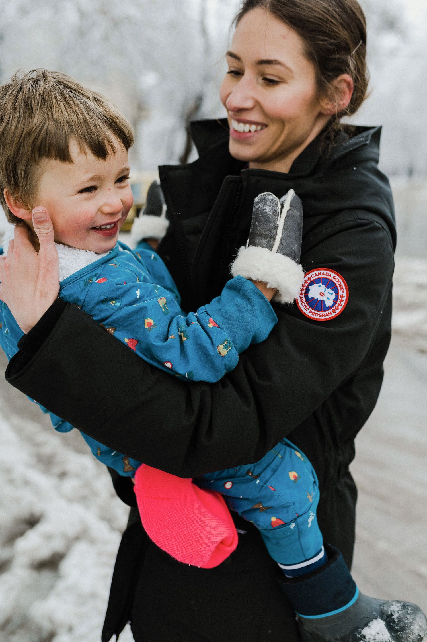 A parent and child share joyful moments playing together in the snow while wearing winter coats.